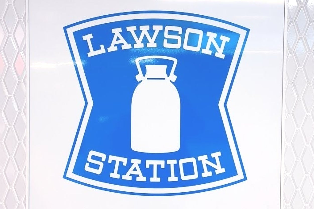 白い壁に「LAWSON STATION」と書かれた青い看板。中央にはミルク缶の絵が描かれている。