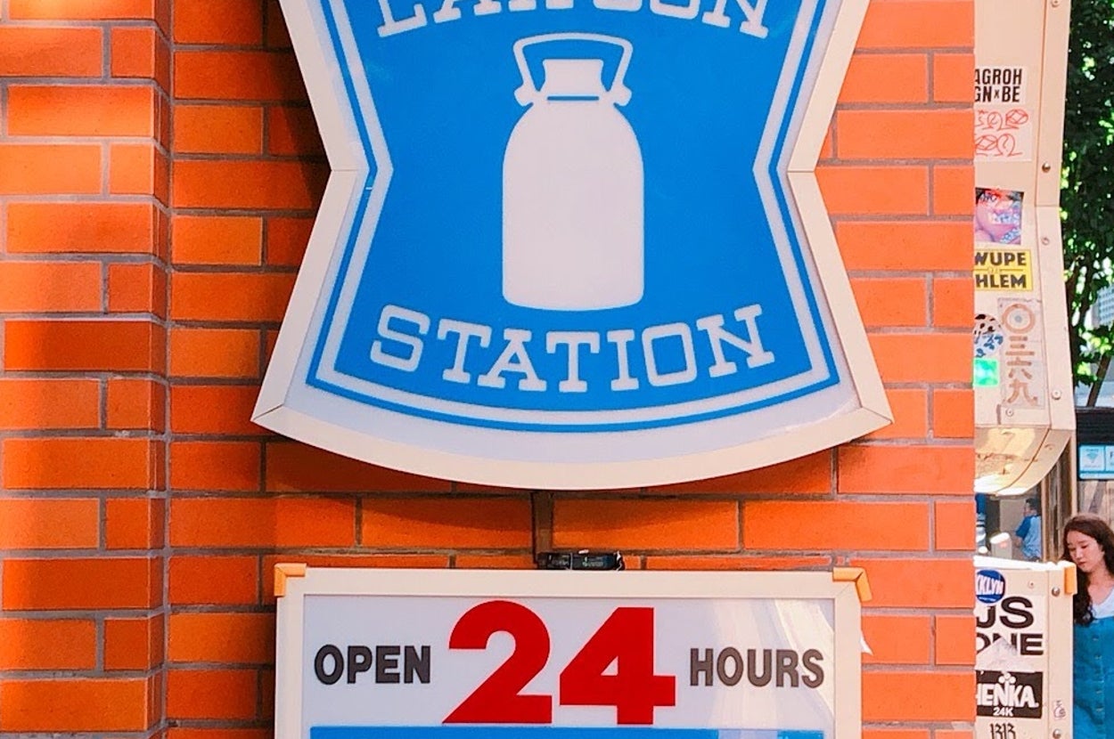 青地に白の牛乳瓶が描かれた「LAWSON STATION」看板。24時間営業の案内付き。