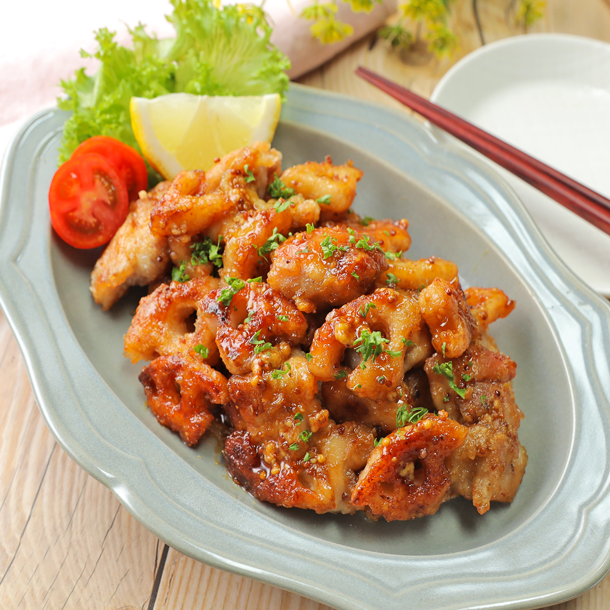 お皿に盛られた唐揚げに、レモンとトマトの付け合わせ。食卓に置かれた箸が見える。