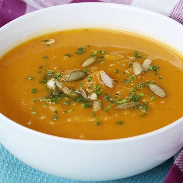 Bowl of creamy pumpkin soup topped with pumpkin seeds and chives