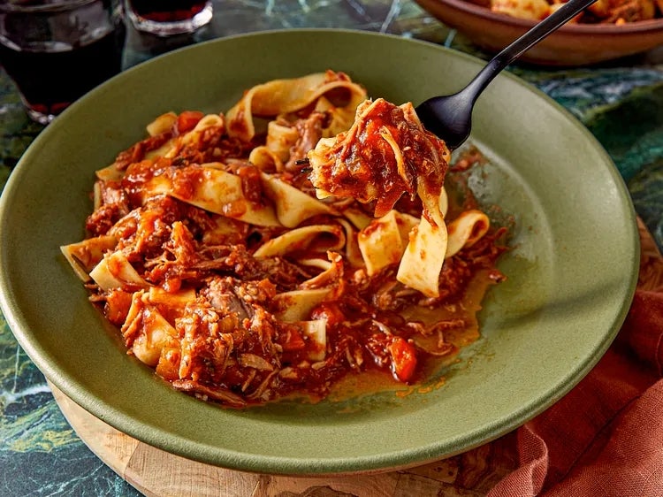 Plate of pasta with rich meat sauce, fork lifting a bite. Cozy meal setting
