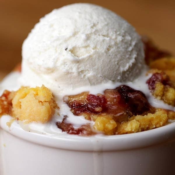 Ice cream scoop atop berry crumble in a white bowl, melting slightly