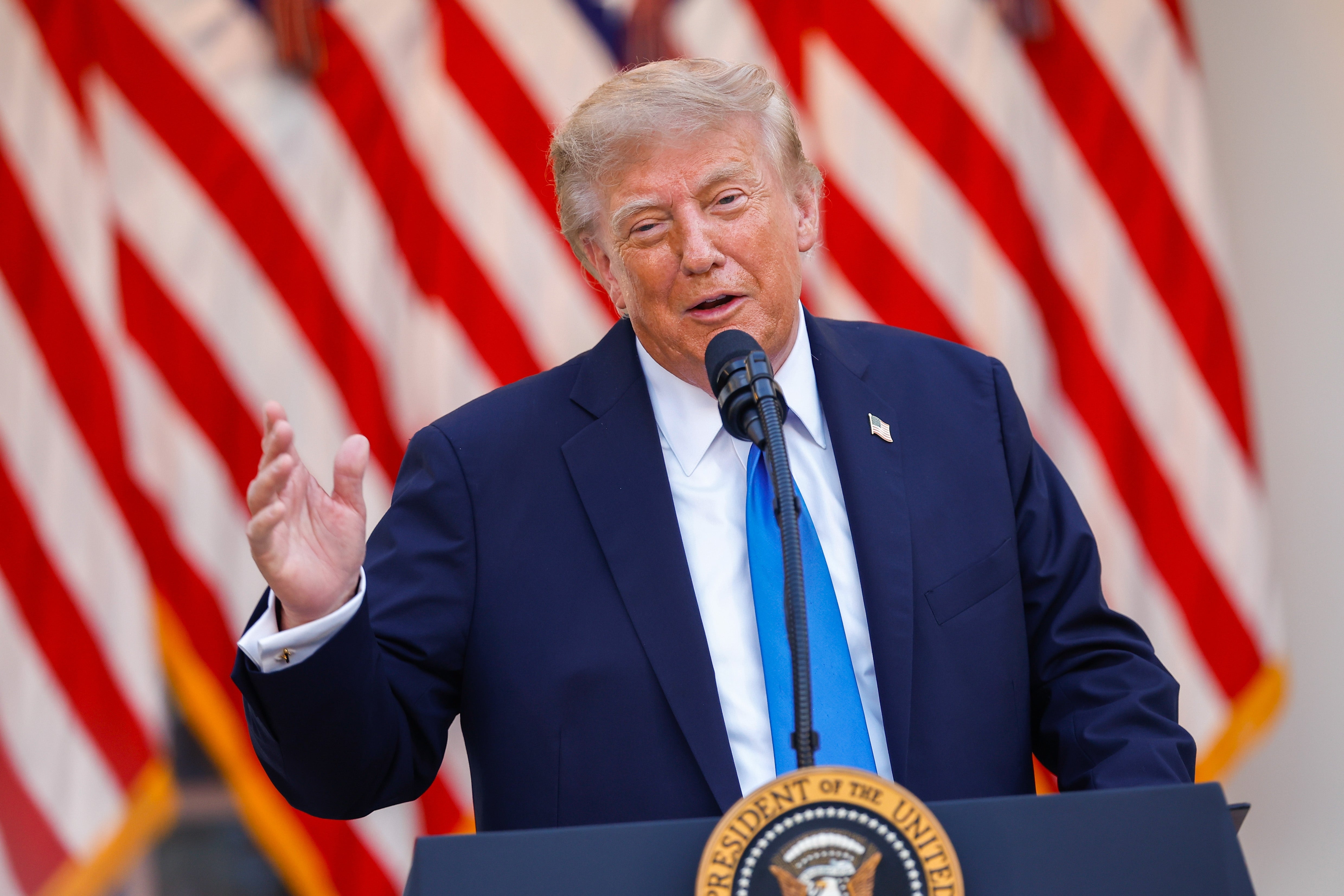 En person snakker ved et podium med en mikrofon og gestikulerer med en hånd. Amerikanske flagg vises i bakgrunnen