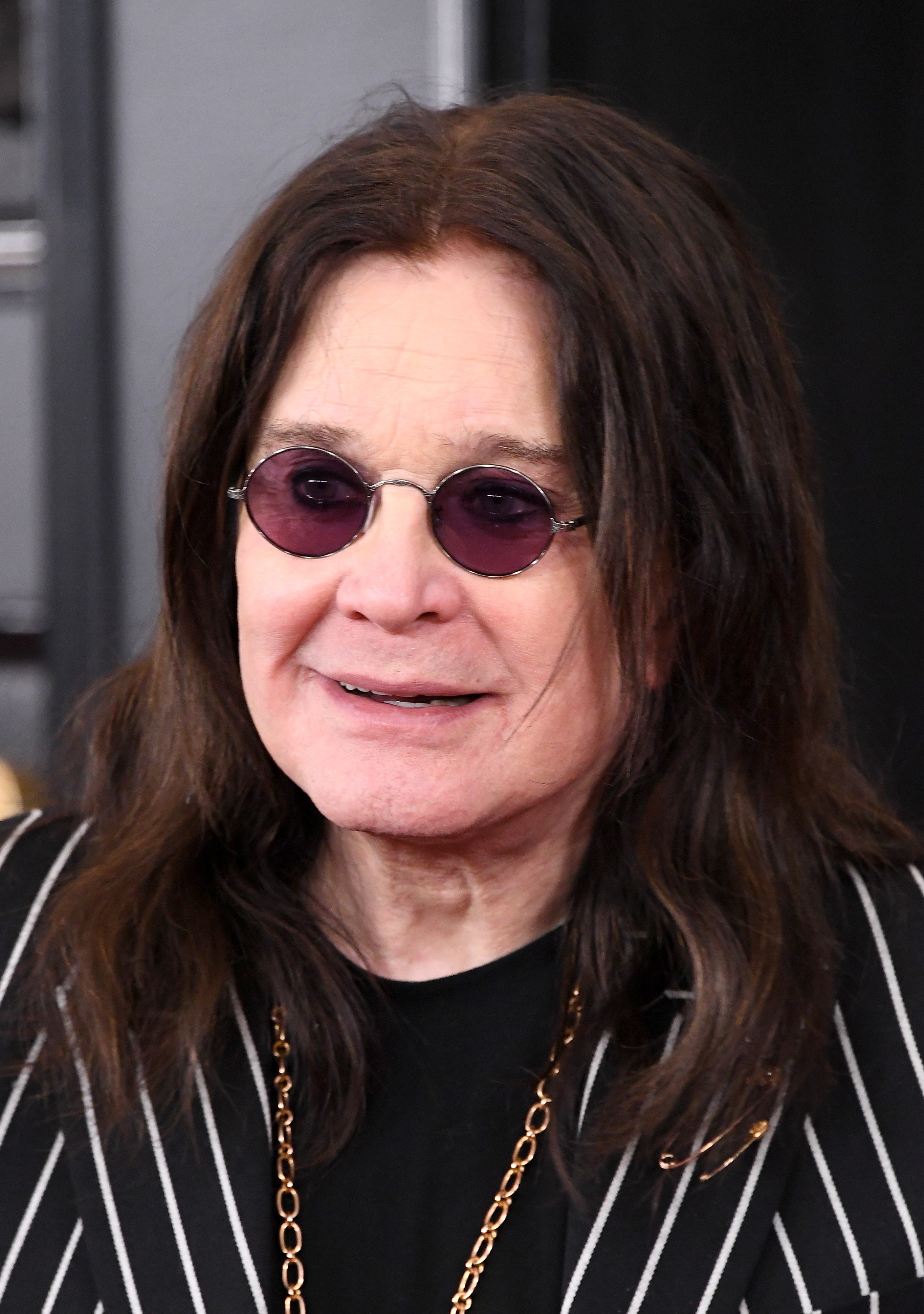 Person with long hair wearing round sunglasses and a pinstripe jacket, smiling
