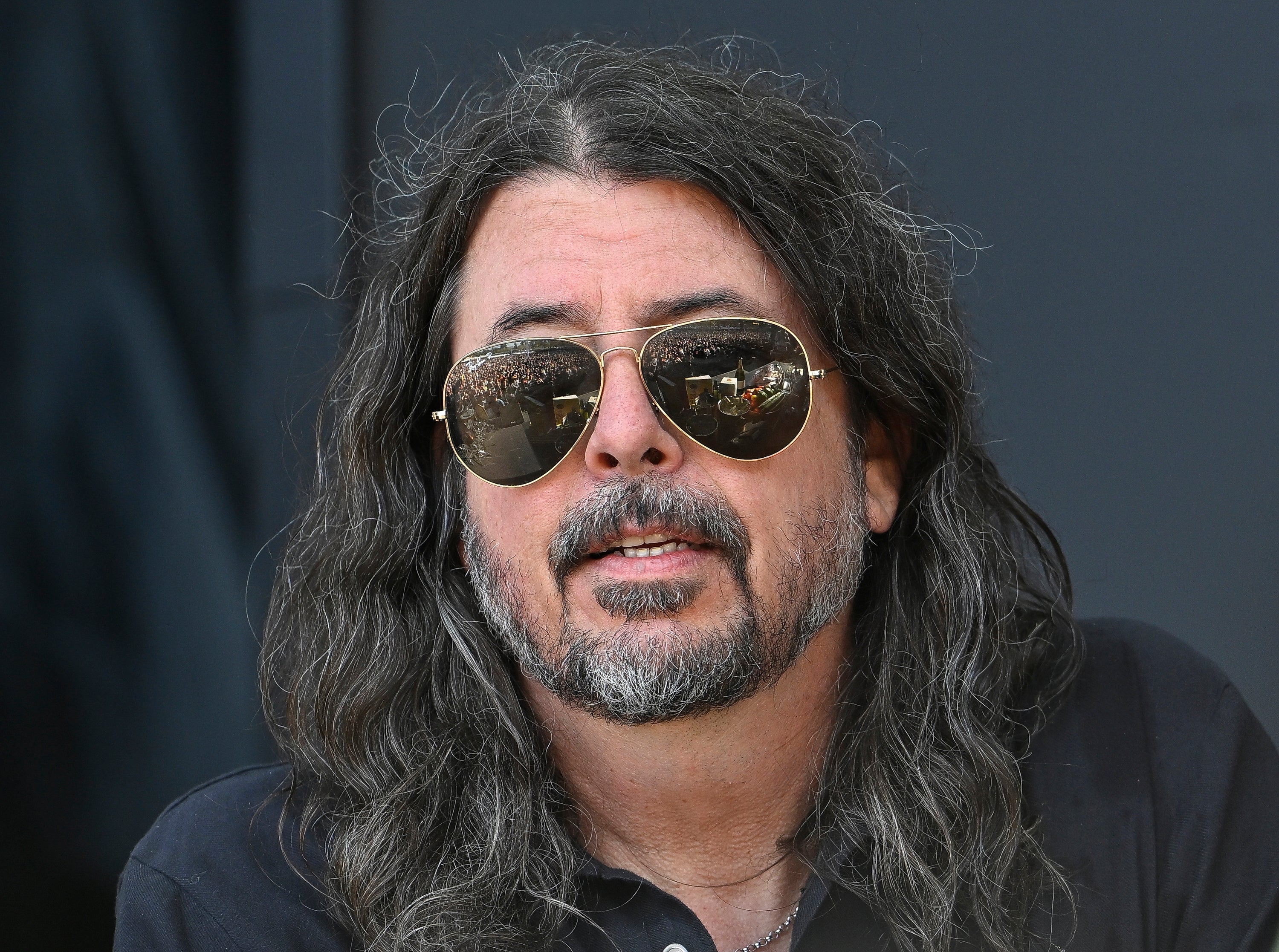 Person with long hair and sunglasses, wearing a collared shirt, looking ahead
