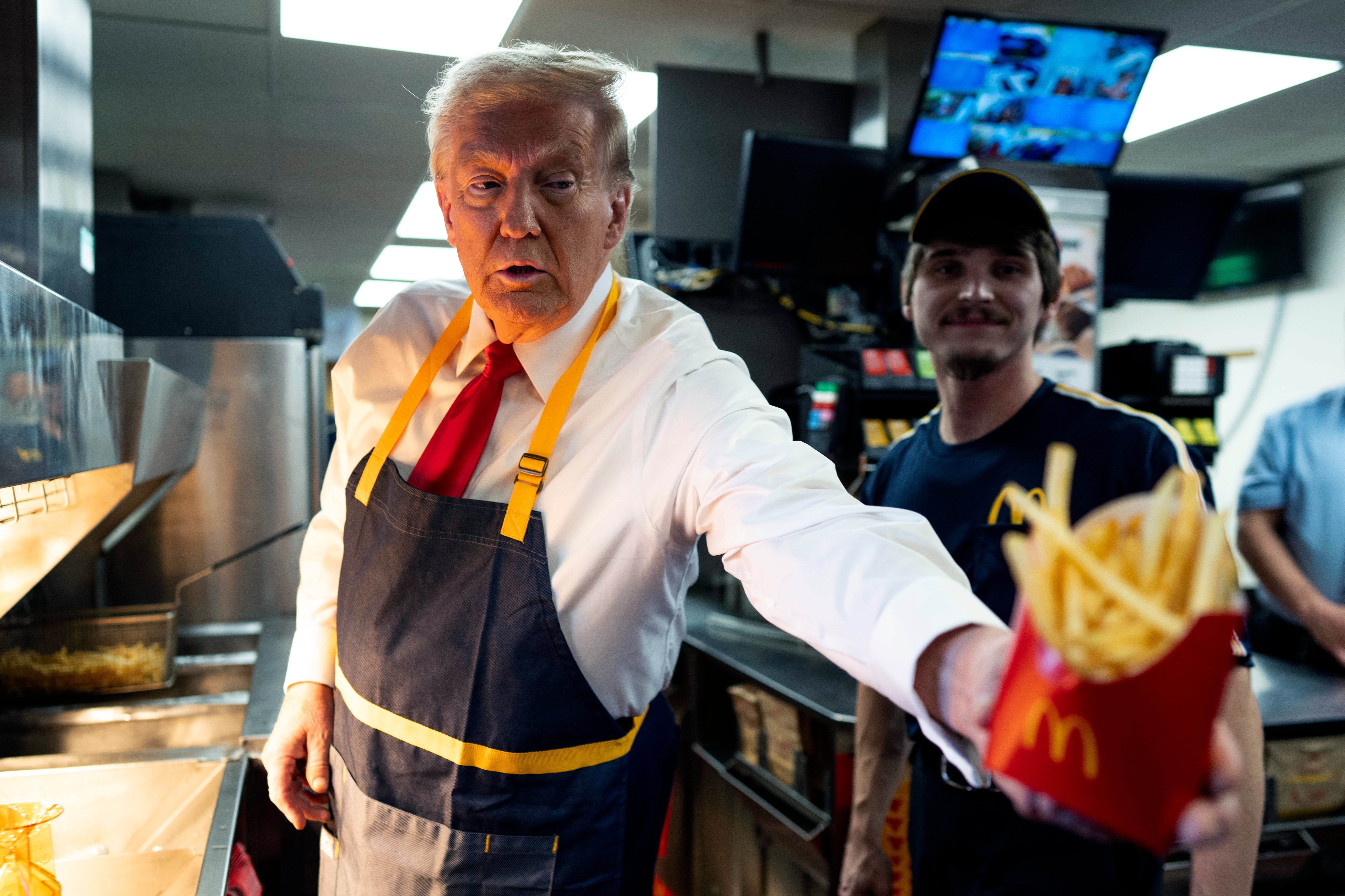 En person på et gatekjøkken med forkle deler ut pommes frites. En annen arbeider i uniform står like ved i bakgrunnen