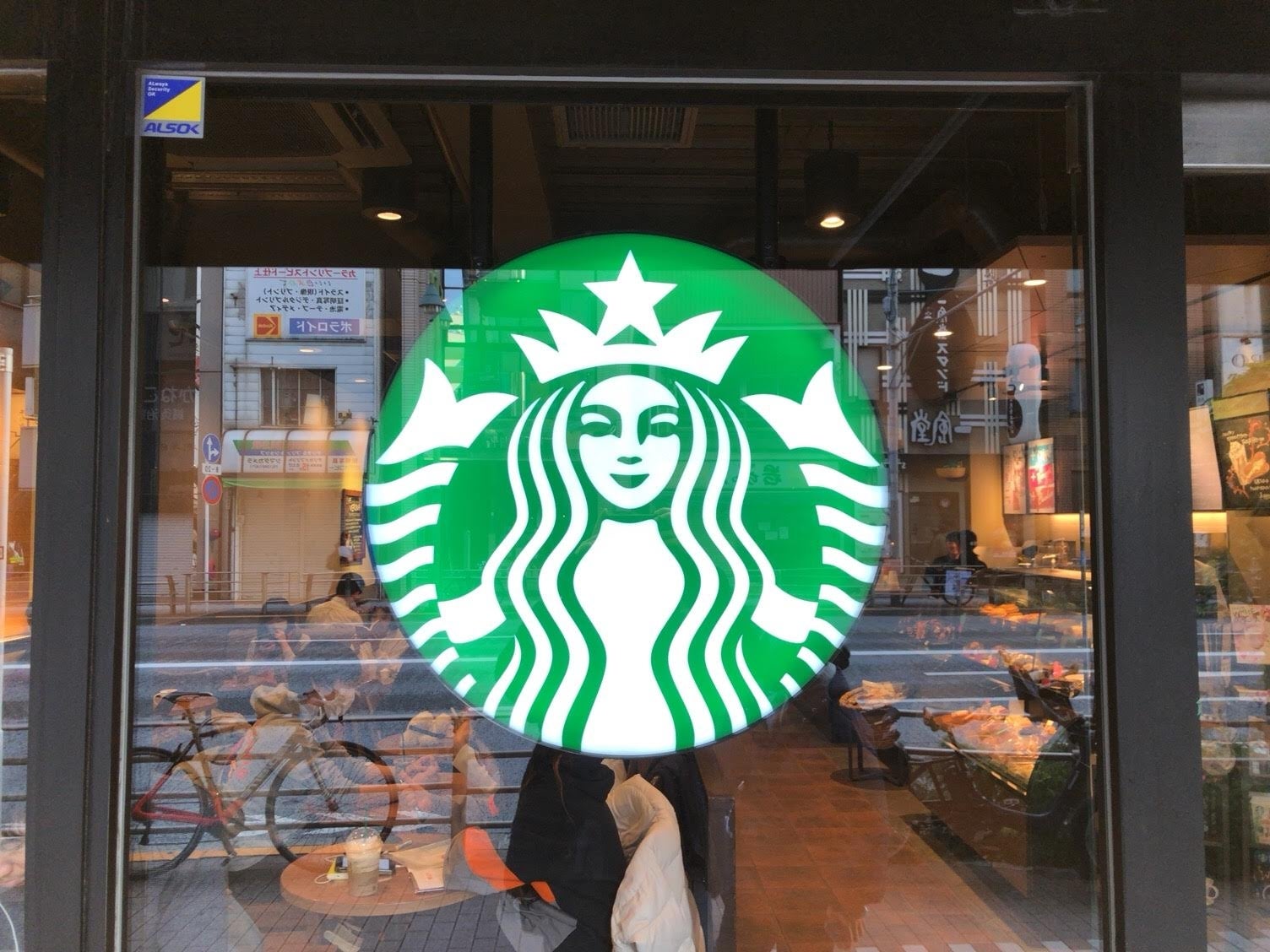 スターバックスのロゴがガラス窓に表示されているカフェの外観。背景には通りの風景が見える。