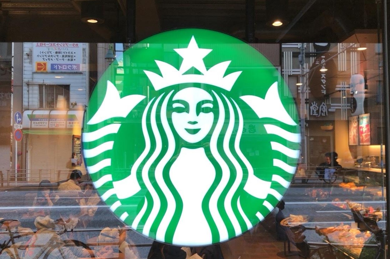 スターバックスのロゴがガラス窓に表示されているカフェの外観。背景には通りの風景が見える。