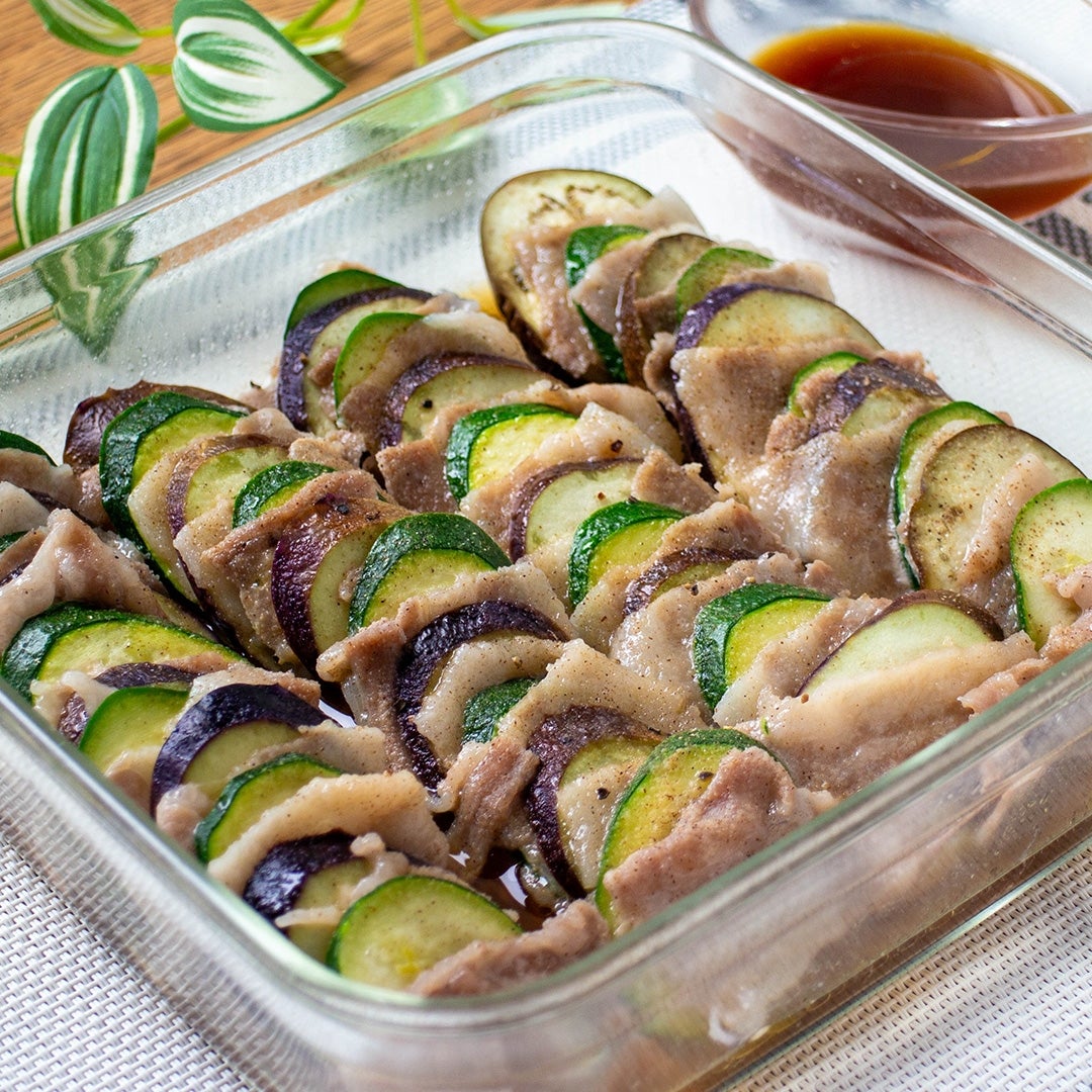 ナスとズッキーニと豚肉を並べた料理、ソースが添えられた調理テーブルの上にある。