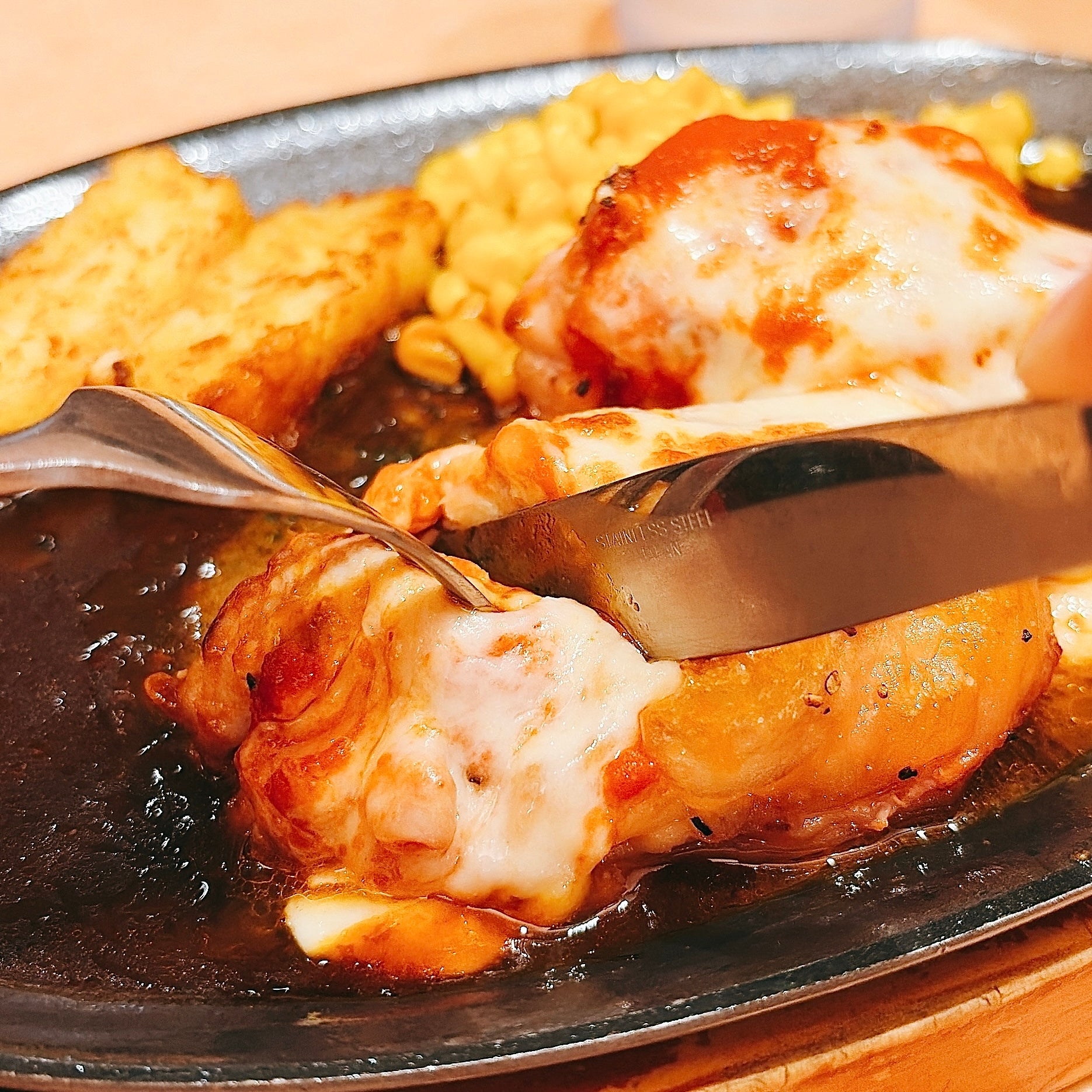 サイゼリヤ「柔らかチキンのチーズ焼き」チキンをフォークとナイフで切る様子。