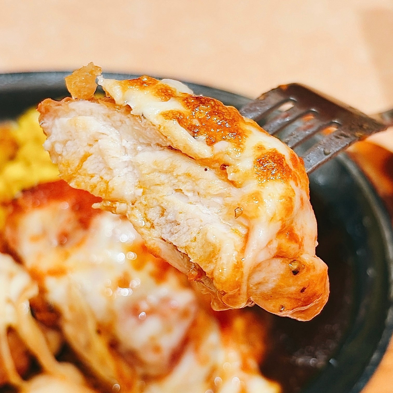 サイゼリヤ「柔らかチキンのチーズ焼き」チーズがトッピングされたチキンがフォークに刺さっている。