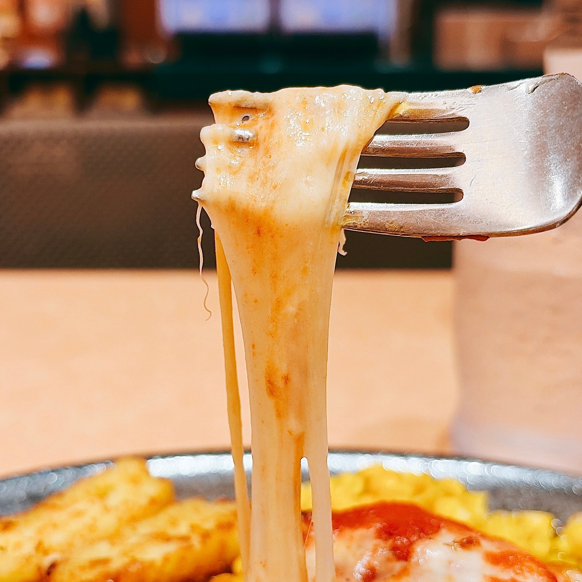 サイゼリヤ「柔らかチキンのチーズ焼き」フォークで持ち上げたチーズがとろける様子。