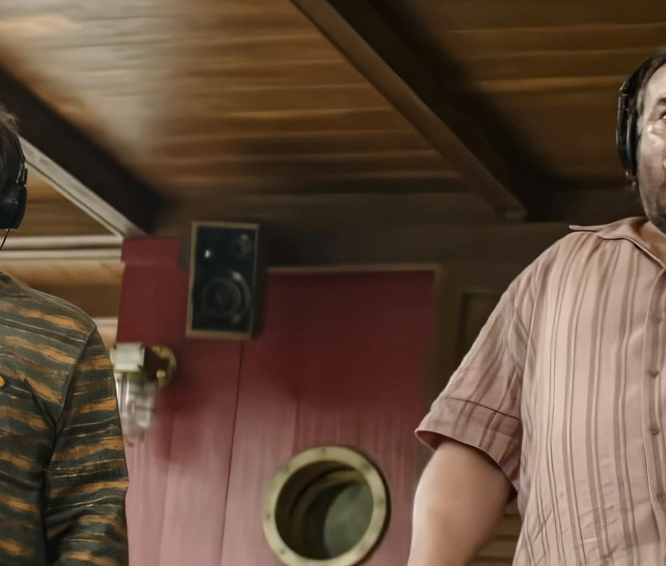 Two people with headphones look surprised while recording audio indoors. One wears a striped sweater, the other a striped shirt