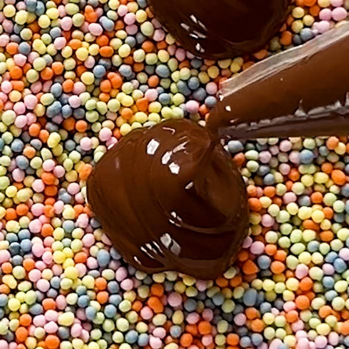 チョコレートの絞り袋でカラフルな小粒スプリンクルの上にチョコレートを絞っている様子。