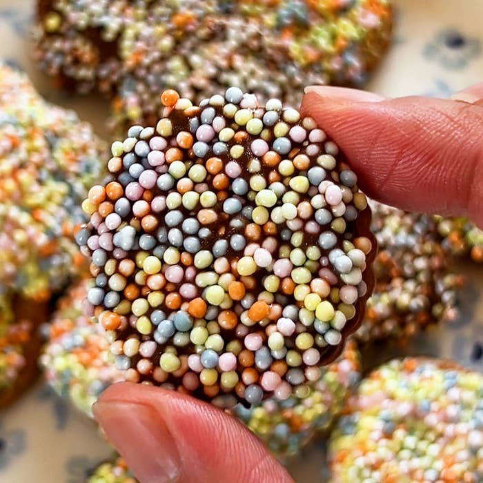 指で持ったチョコレート菓子に、カラフルなスプリンクルがトッピングされています。