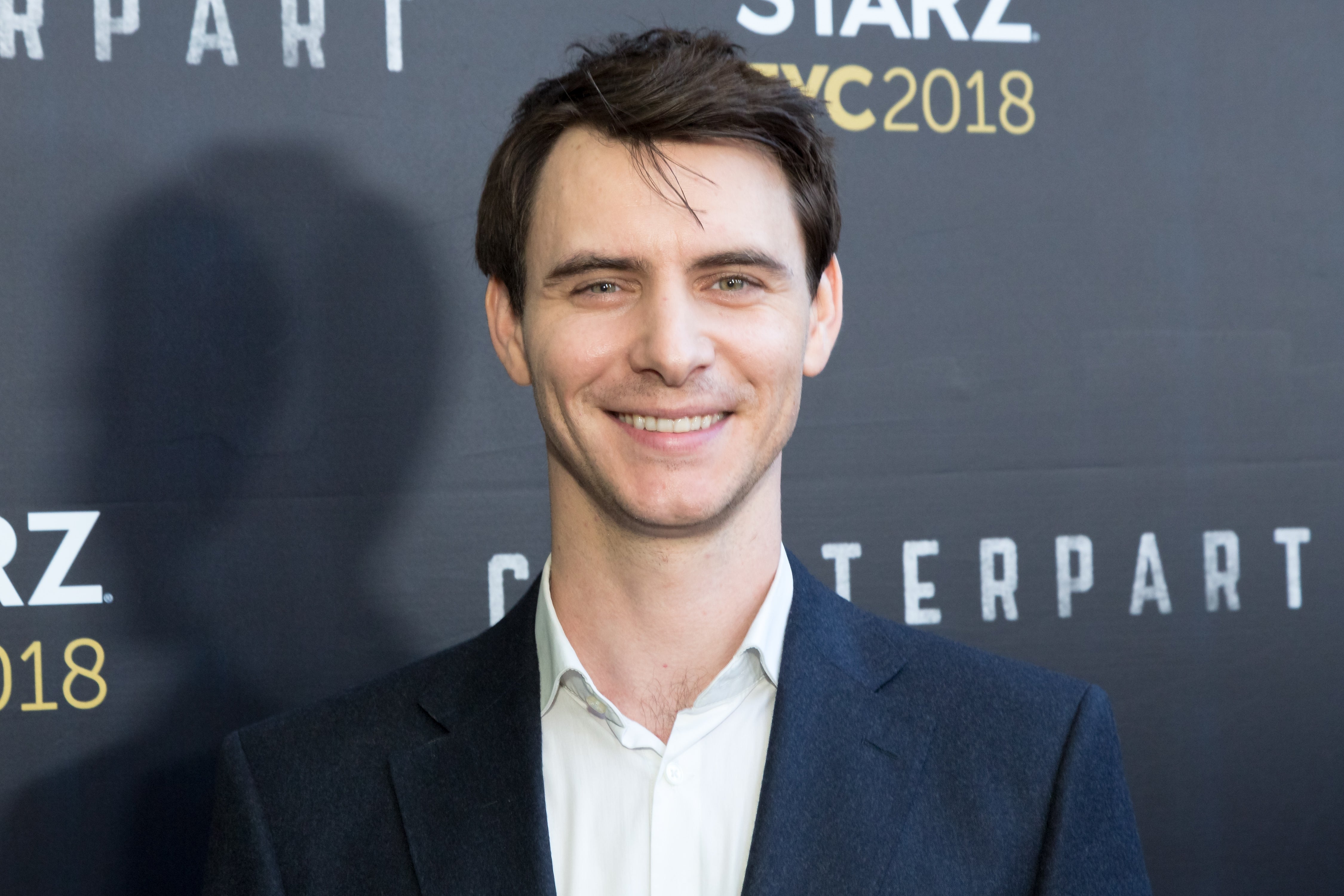 Mann som smiler på et Starz NYC 2018-arrangement i dress og hvit skjorte
