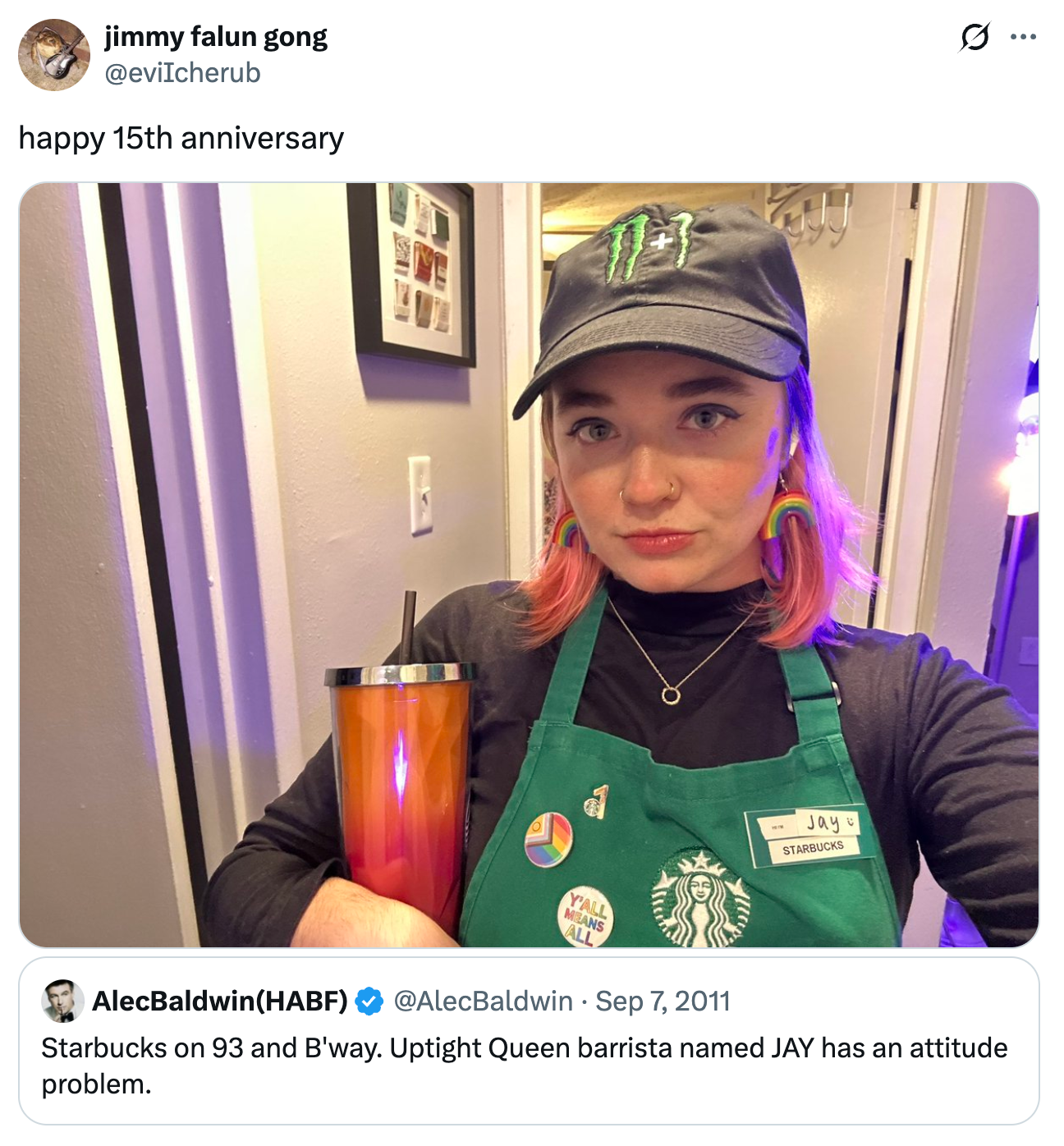 Person i Starbucks-forkle og hatt som holder en drikkeglass, poserer med et nøytralt uttrykk. Navneskiltet lyder