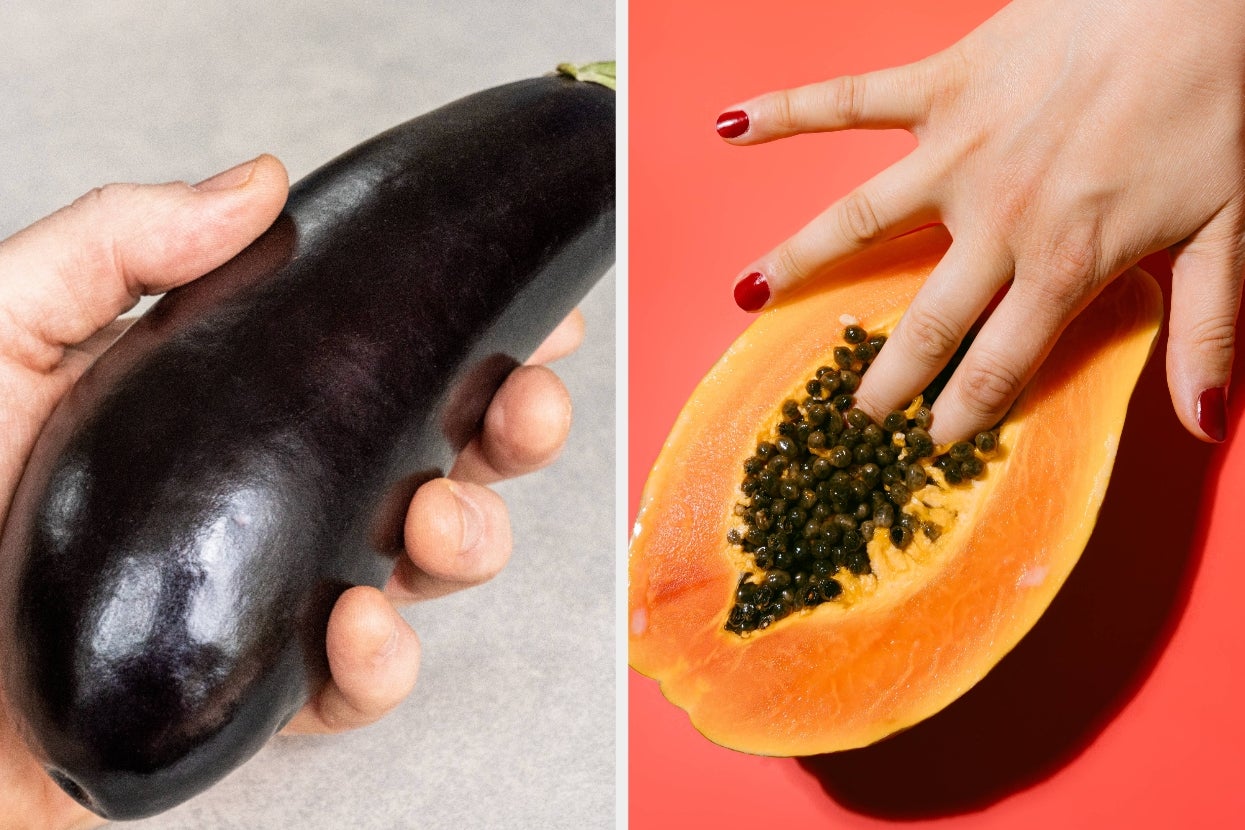 Hand holding an eggplant beside a hand posed in a suggestive gesture over a halved papaya with seeds visible