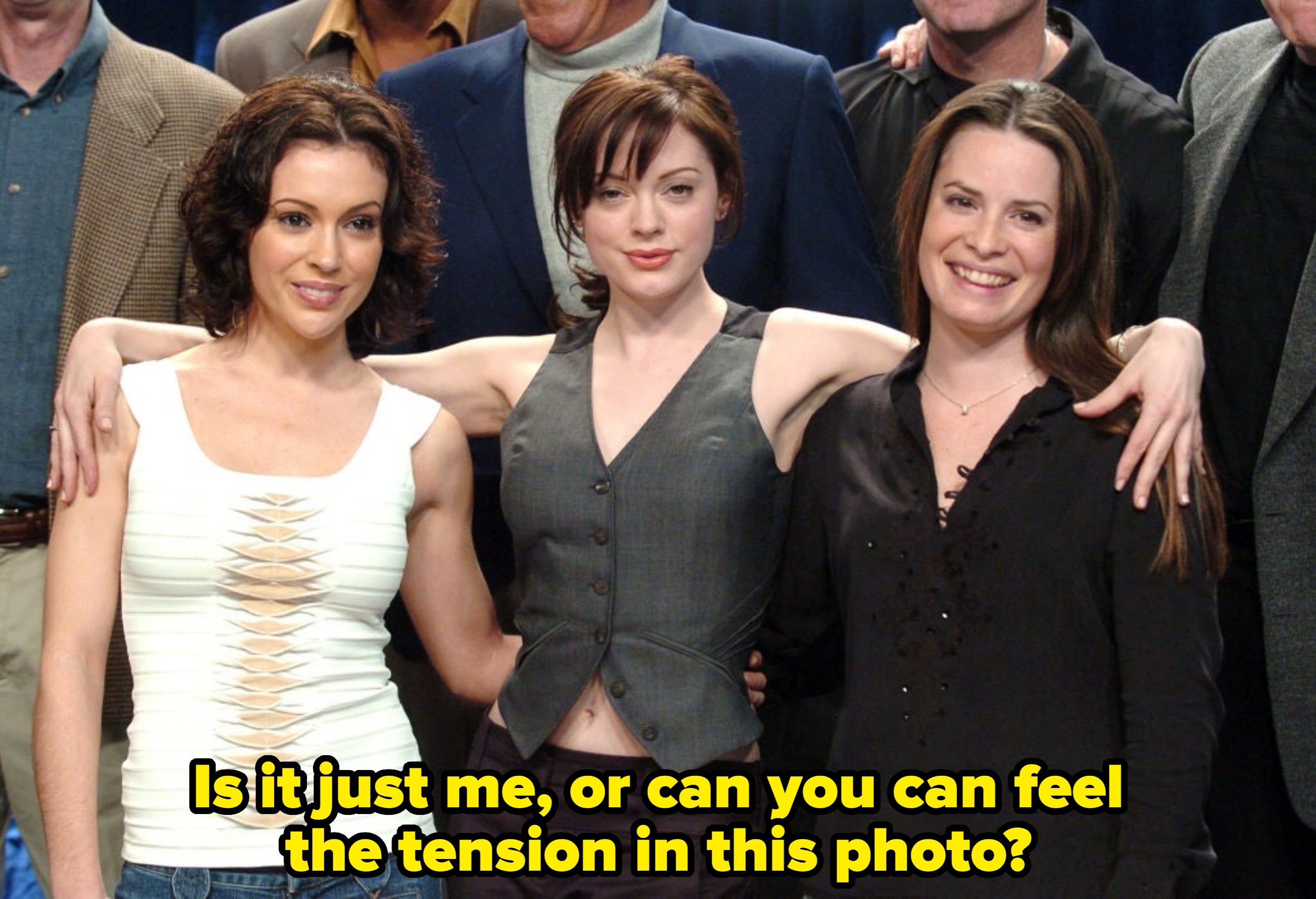 Three people with arms around each other, smiling. One wears a white top, one a sleeveless vest, and one a black blouse. Group photo poses