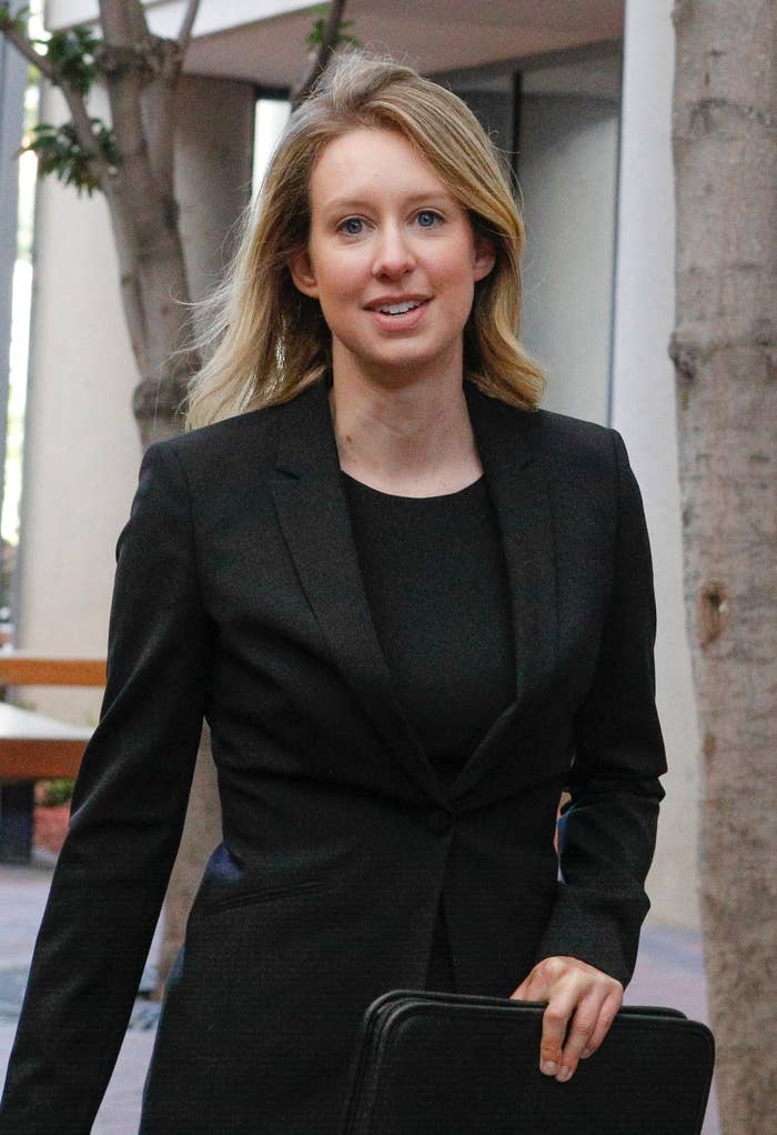 Elizabeth Holmes in business attire walking outdoors, holding a briefcase