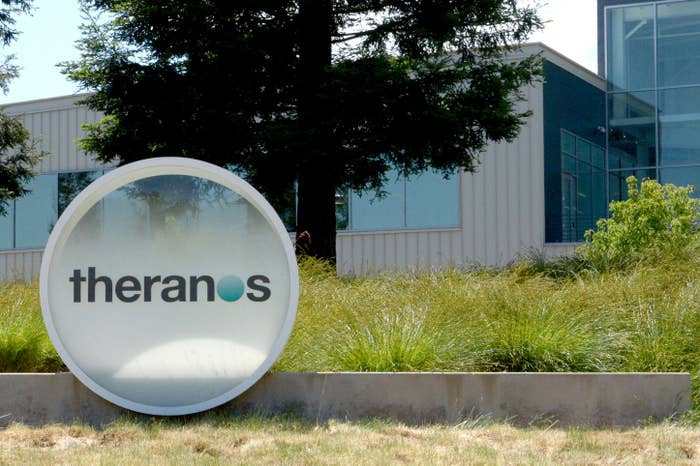 Large sign with "Theranos" in front of a building surrounded by trees and grass