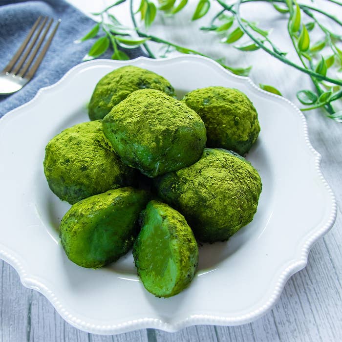 白いプレートに盛られた抹茶をまぶした丸い菓子が6つ。背景に緑の葉飾り。
