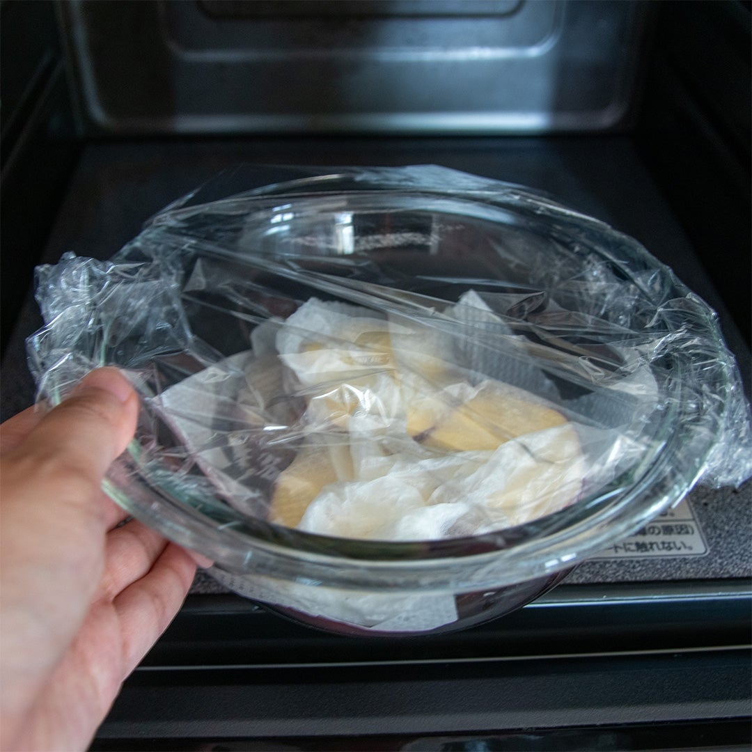 レンジに入れられ、ラップがかけられたガラスボウルの中に、キッチンペーパーに包まれたさつまいもが入っている。