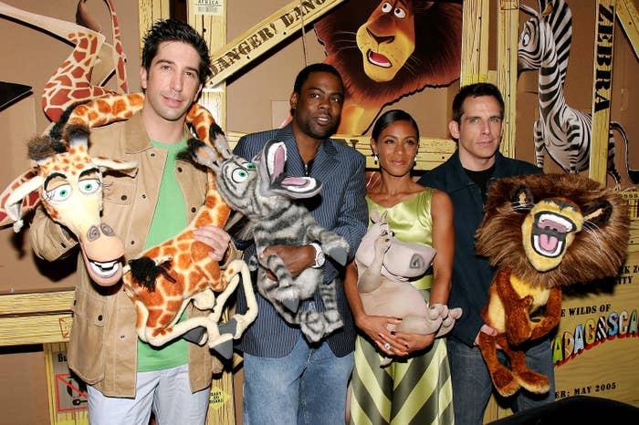 Four people hold plush character props from "Madagascar" at a promotional event. They're dressed in casual and semi-formal attire