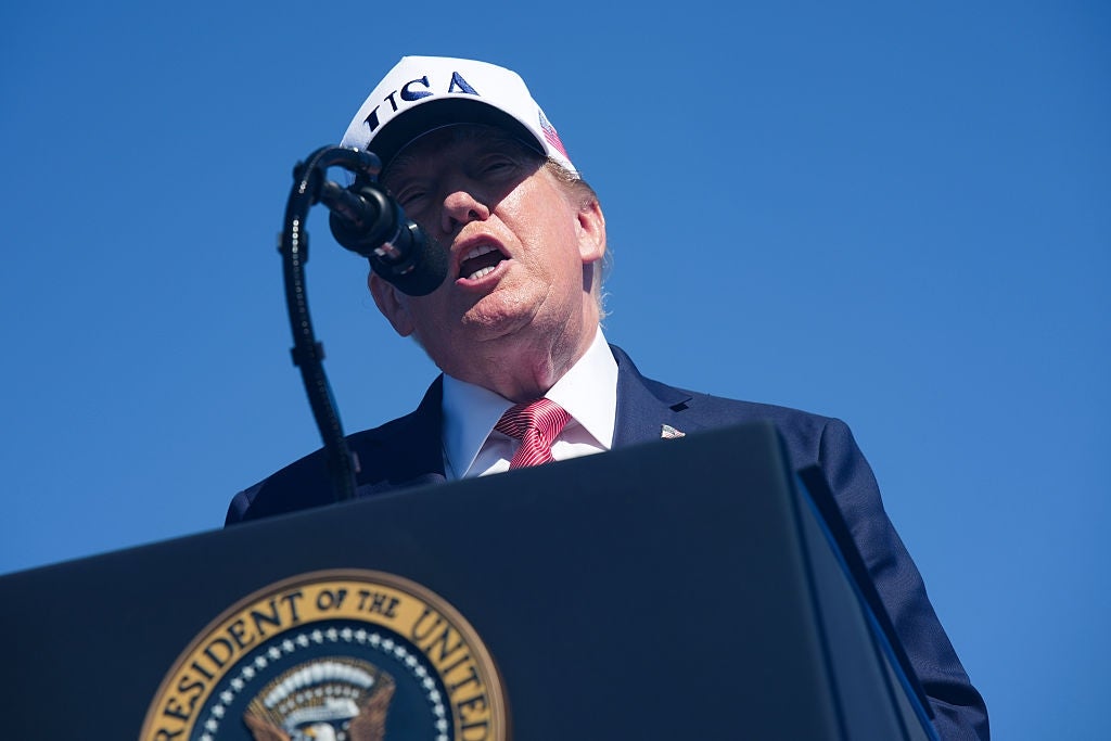En person i dress og hatt snakker på et podium med en presidentsegl, utendørs, sett fra lav vinkel