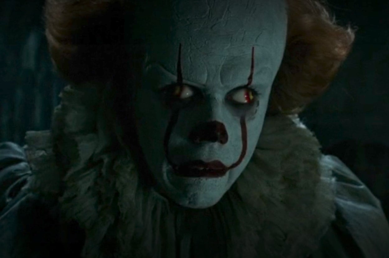 Pennywise from "It" with frizzy hair, exaggerated eyebrows and lips, stares menacingly
