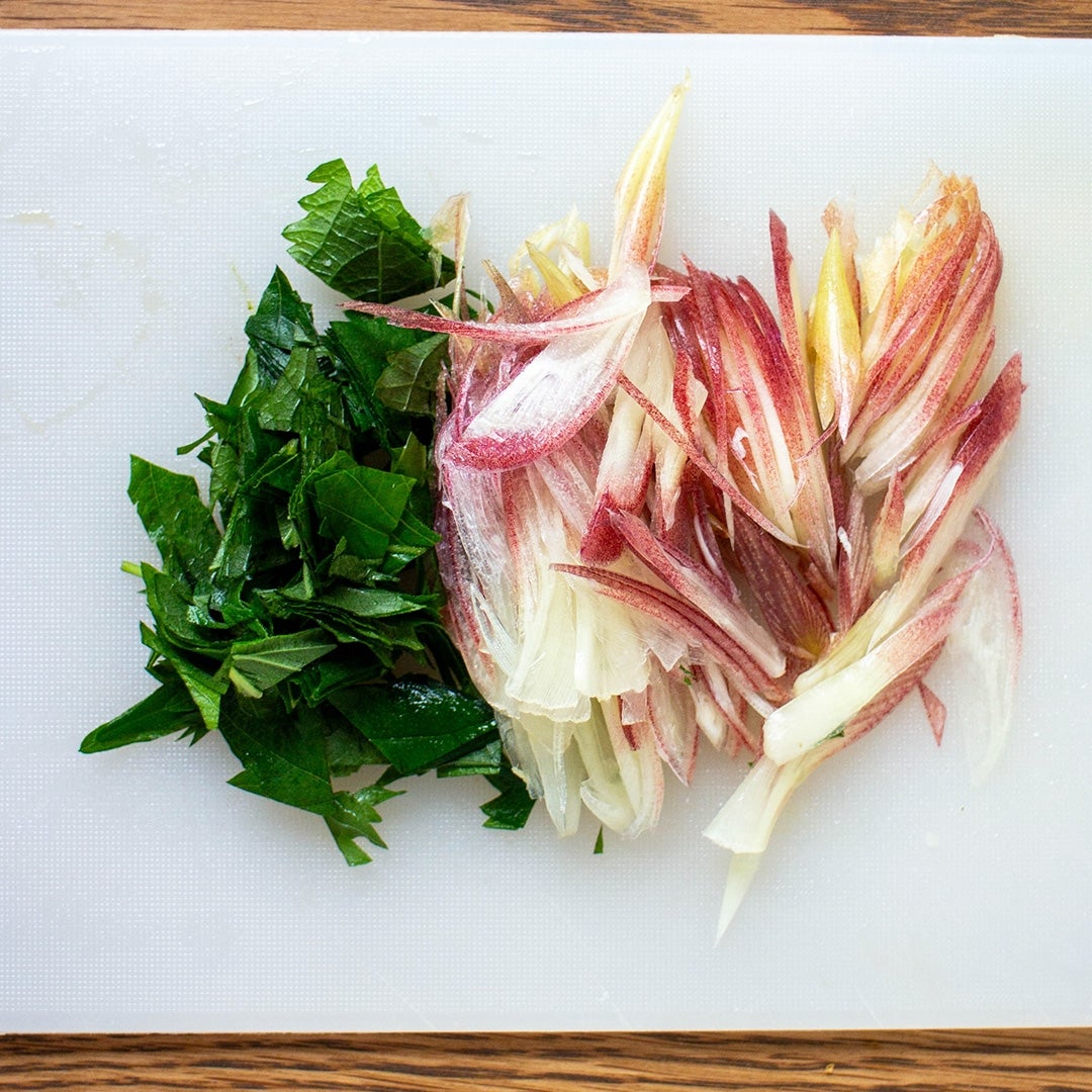 刻んだ野菜がまな板の上に置かれている。左側に緑色の葉、右側に赤みがかった野菜。