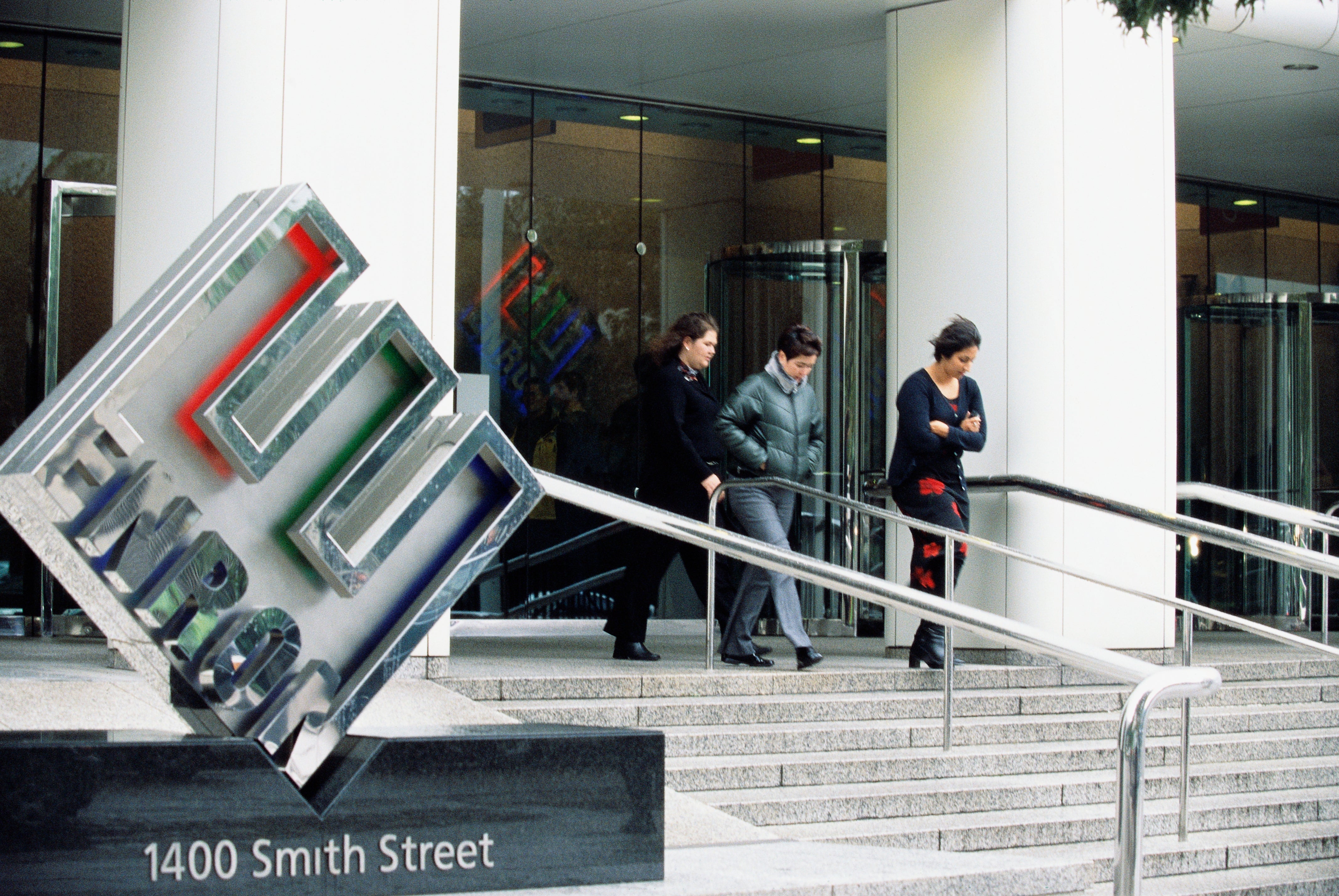 People walking down steps outside a building with an Enron sign. Address plaque reads "1400 Smith Street."