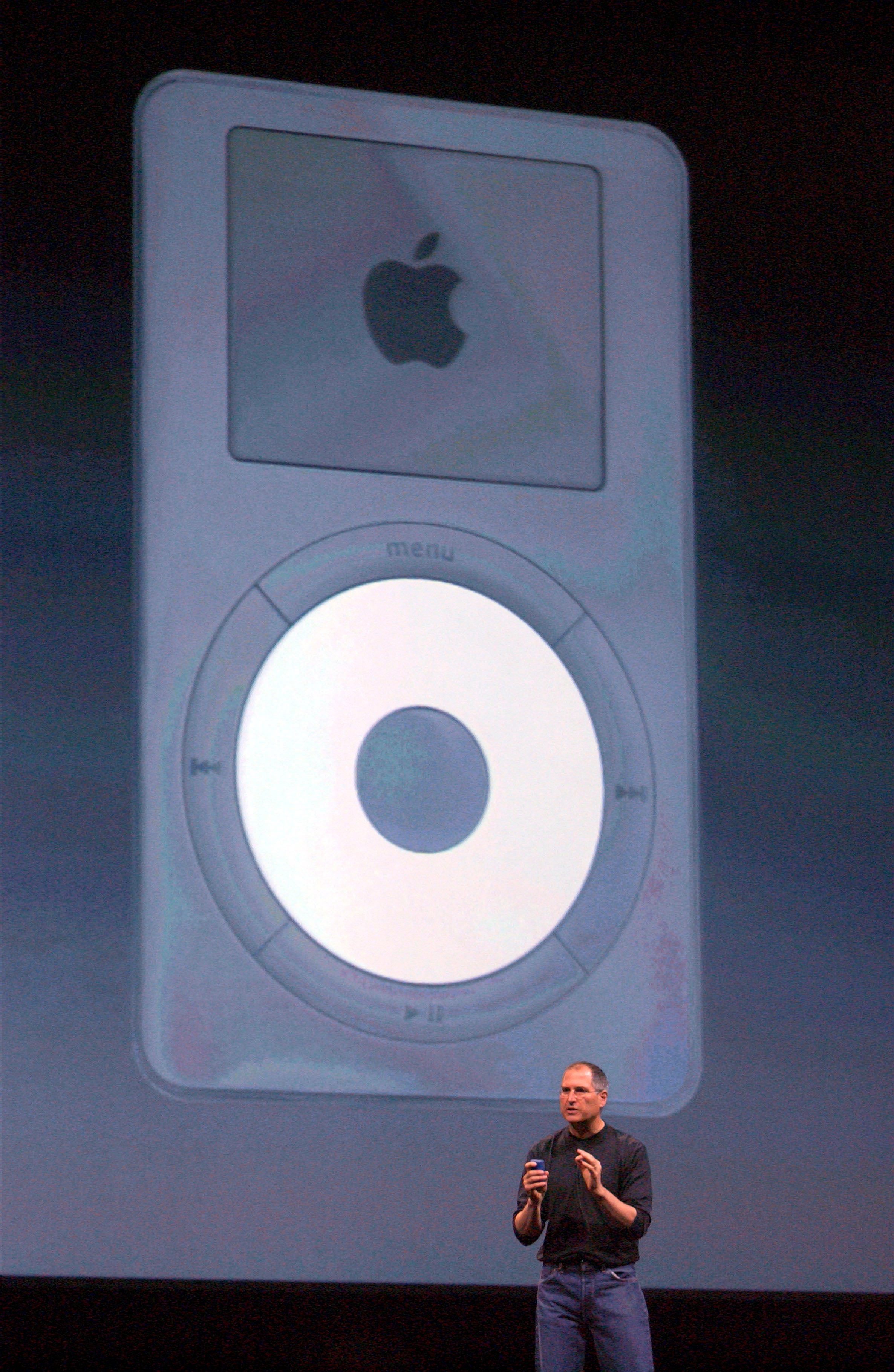A person on stage presents a large image of an early iPod during an event