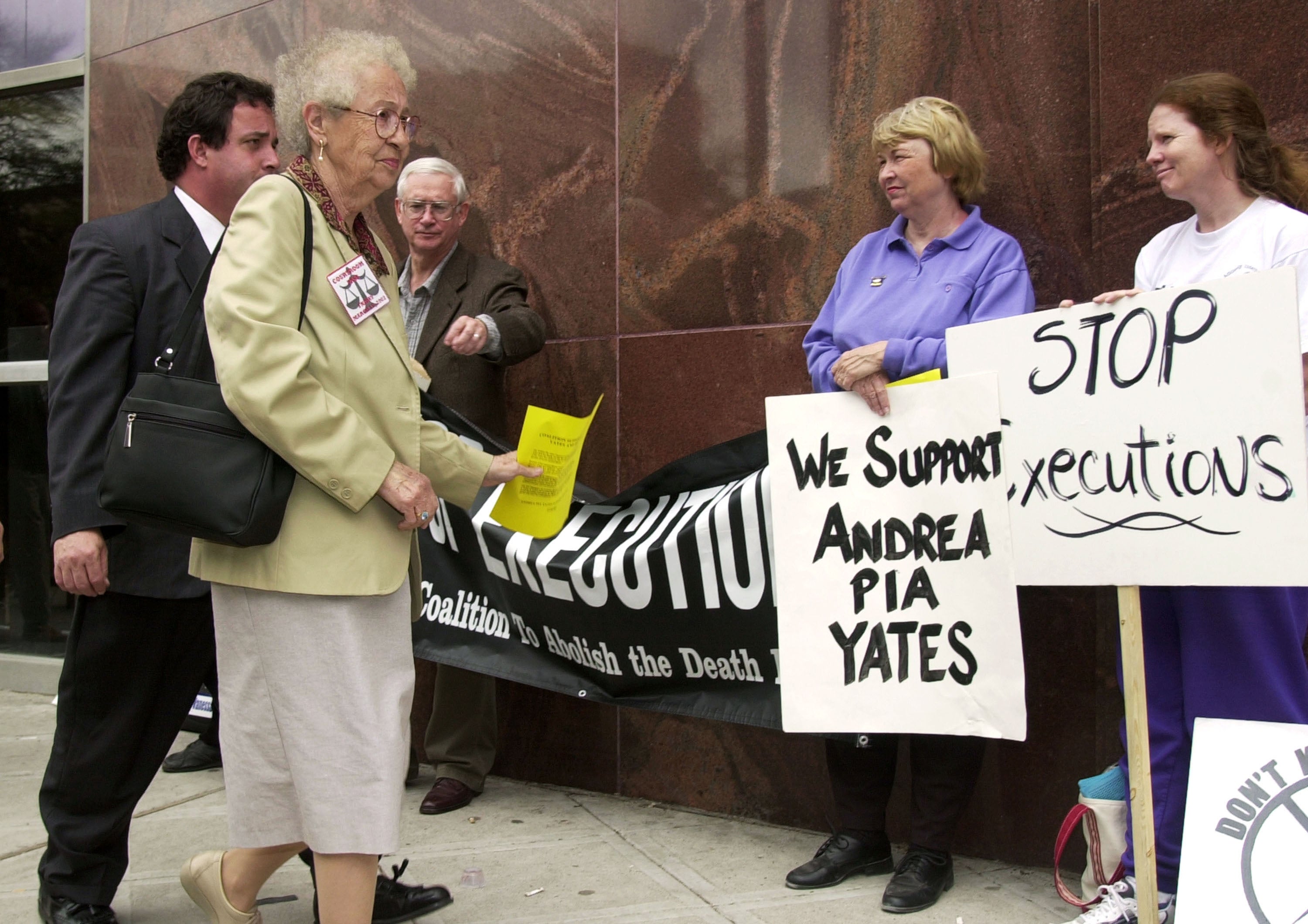 People protest outside a building with signs against executions, supporting Andrea Pia Yates. Three women and one man hold signs and engage with passersby