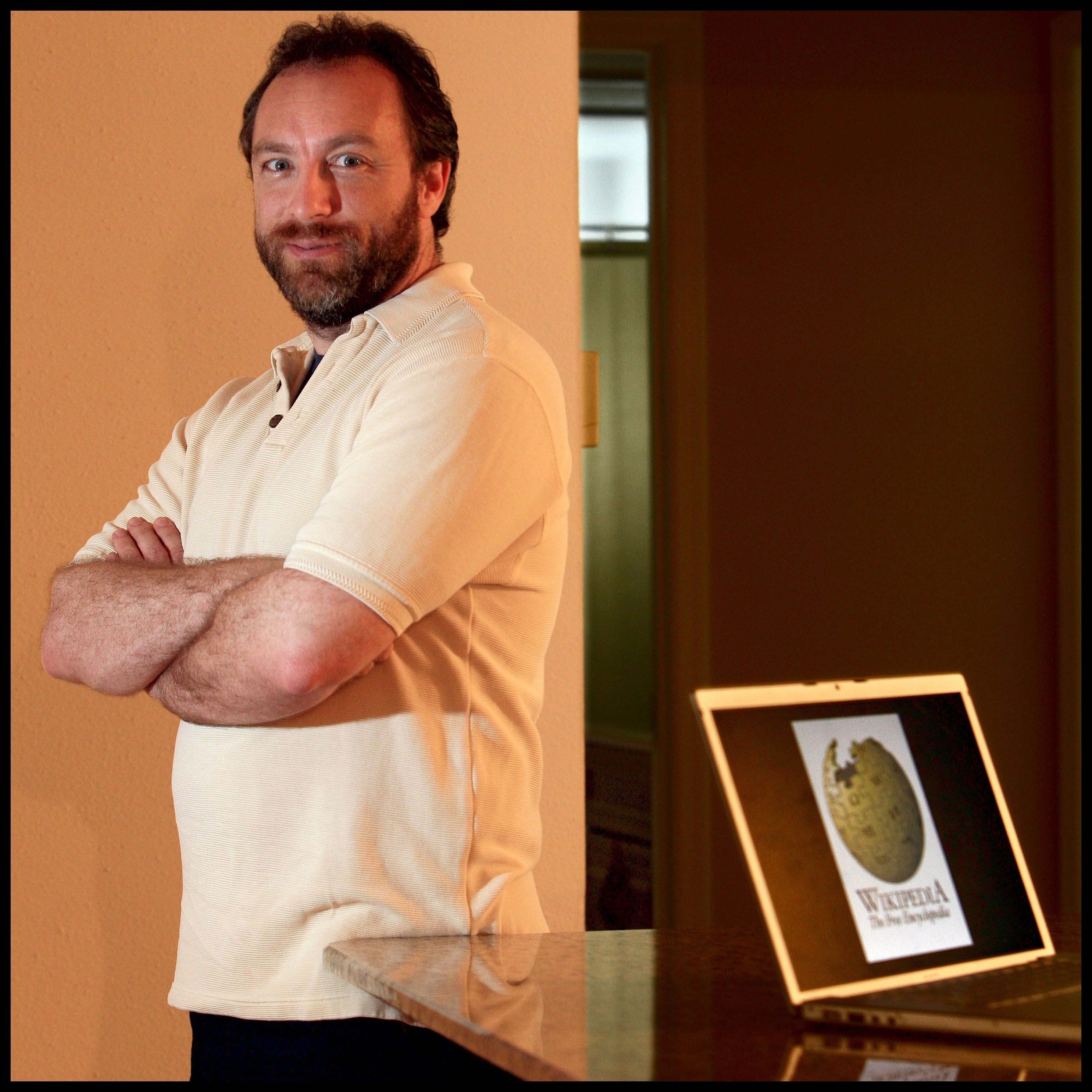 A person stands confidently with arms crossed beside an open laptop displaying the Wikipedia logo