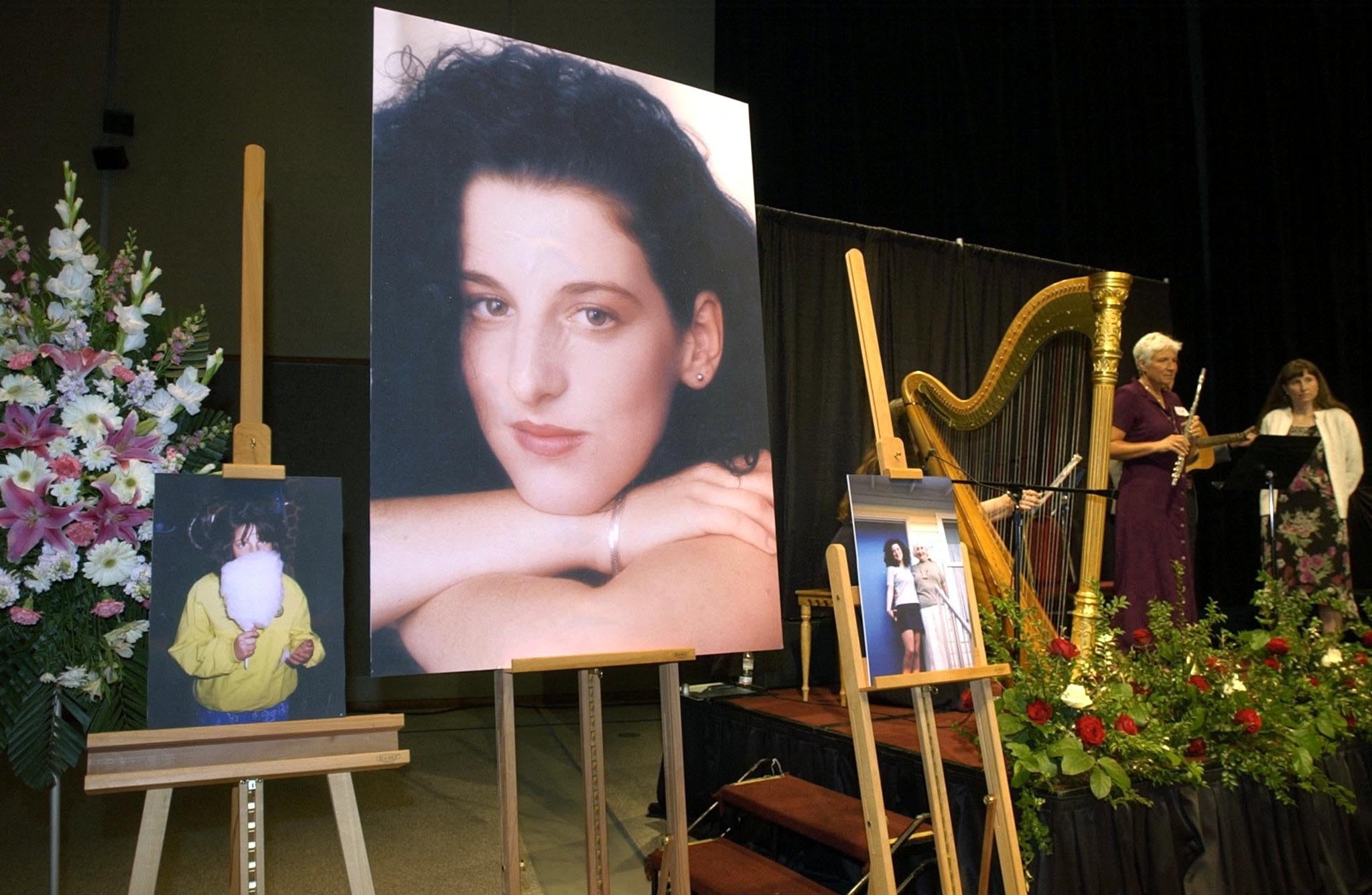 A memorial setup with a large portrait of a woman. Flower arrangements and smaller photos are nearby. A harp and music stand are on stage