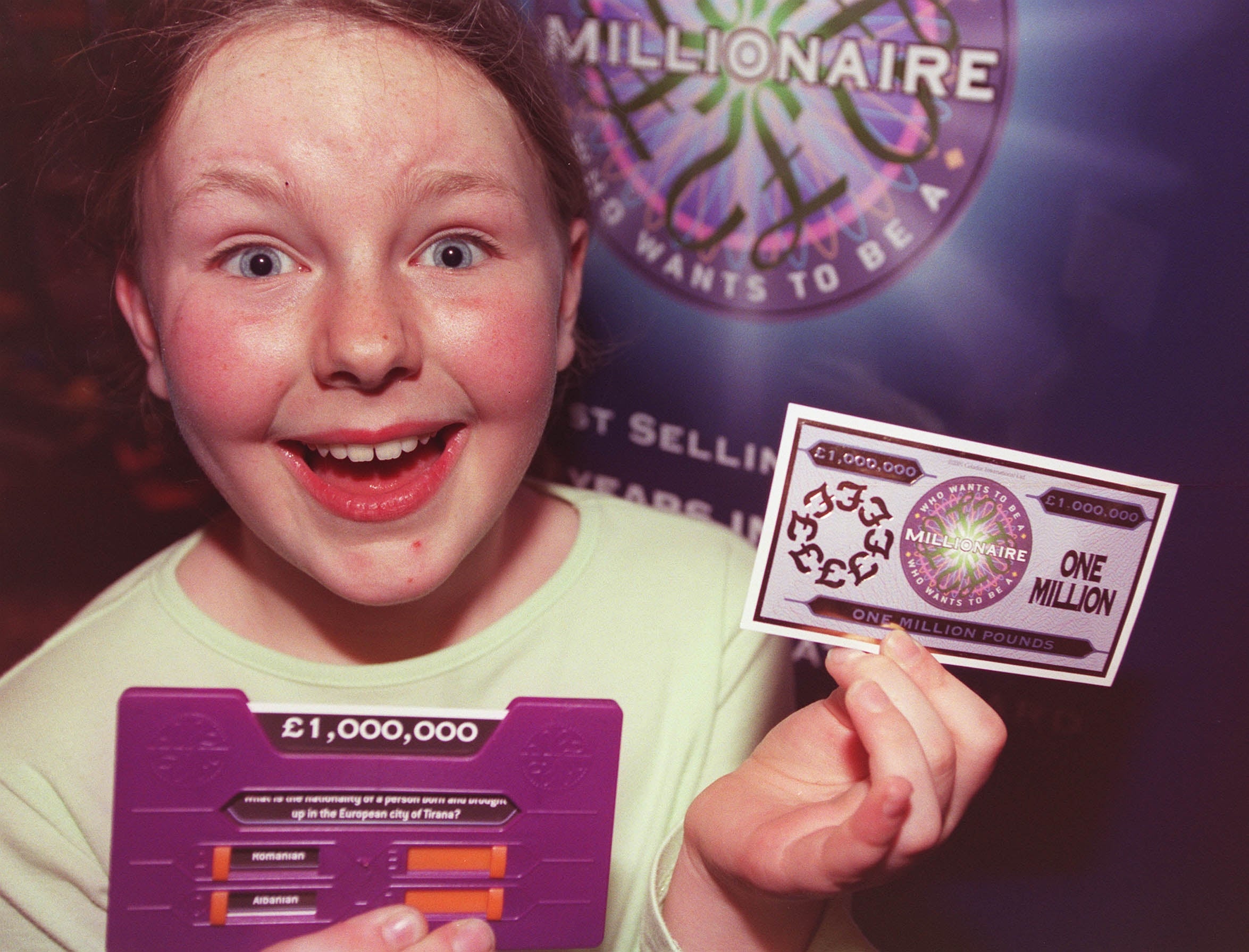 Child holds a toy "Who Wants to Be a Millionaire" set, displaying a mock cheque for one million pounds with excitement