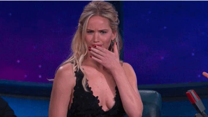 A woman in evening wear makes a surprised expression while sitting on a talk show set