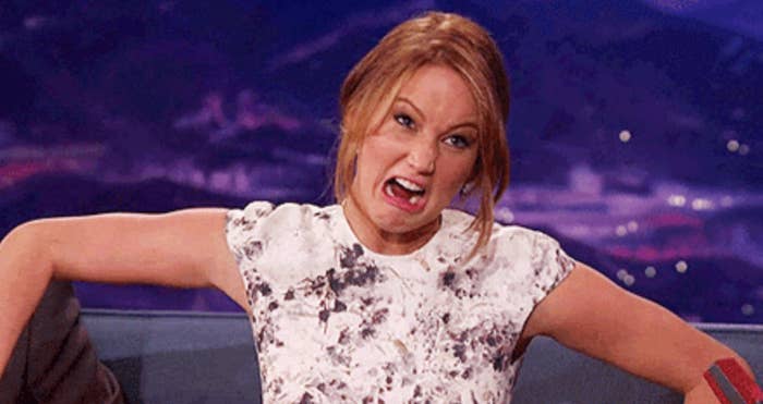 A person on a talk show set makes a playful, exaggerated facial expression while wearing a patterned top