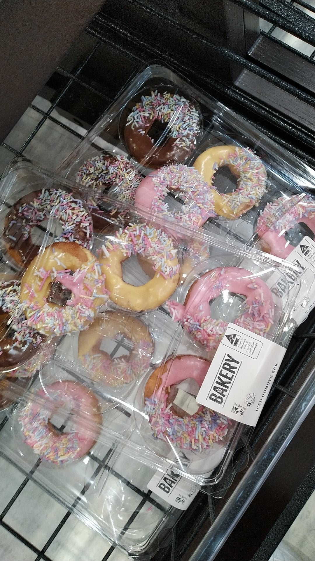 Donuts successful  wide   integrative  containers connected  a shelf, topped with sprinkles. Packaging labeled "Bakery."
