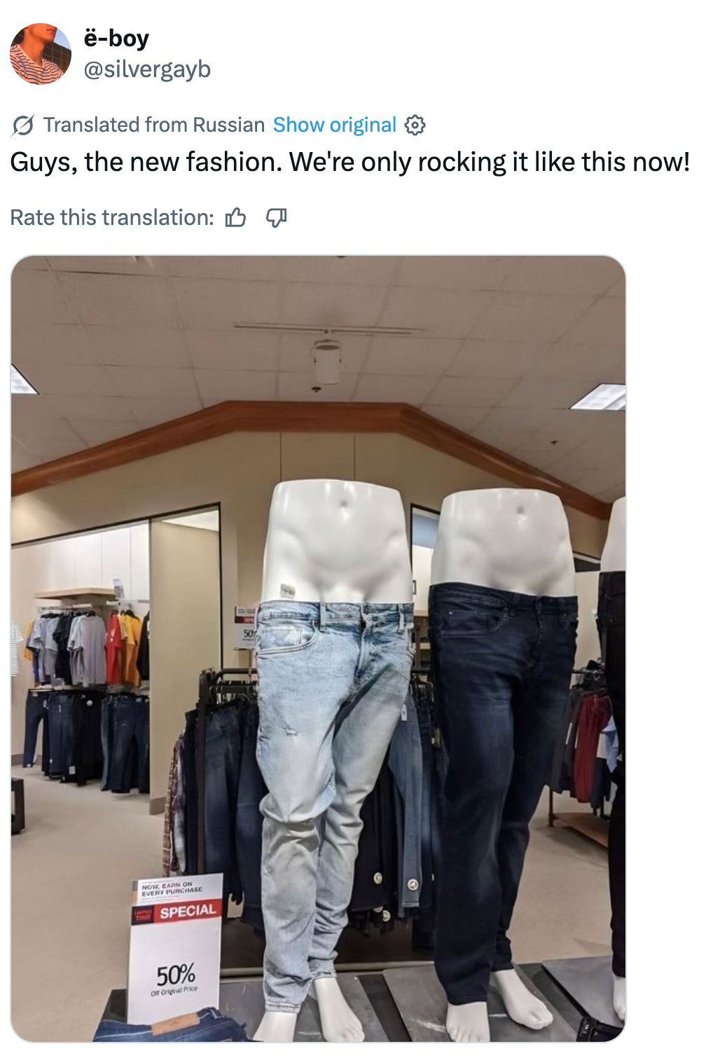 Butikkutstilling med to par jeans på mannekenger uten overkropp, med en humoristisk bildetekst om motetrender