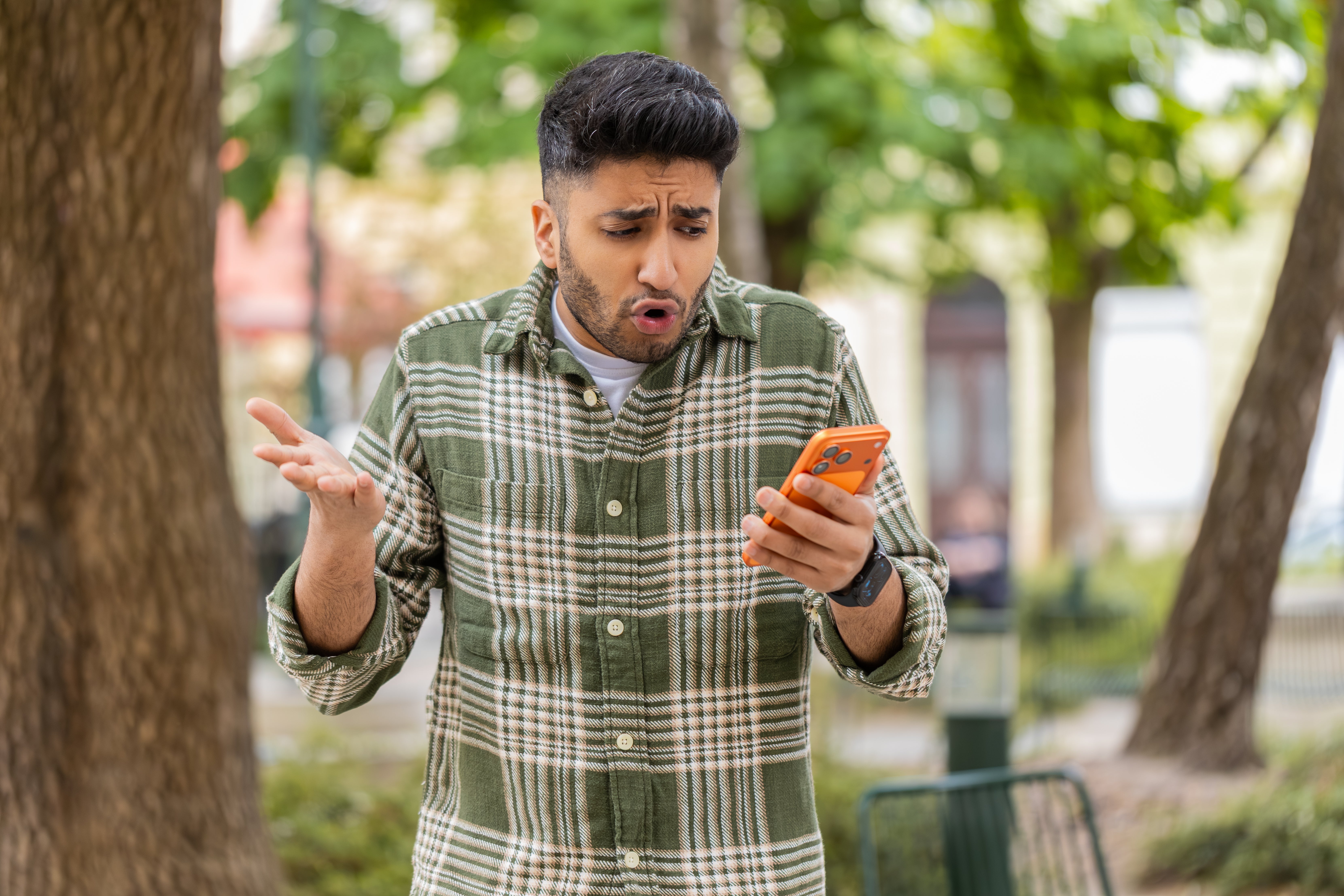 Person outdoors looking surprised at their phone, wearing a plaid shirt