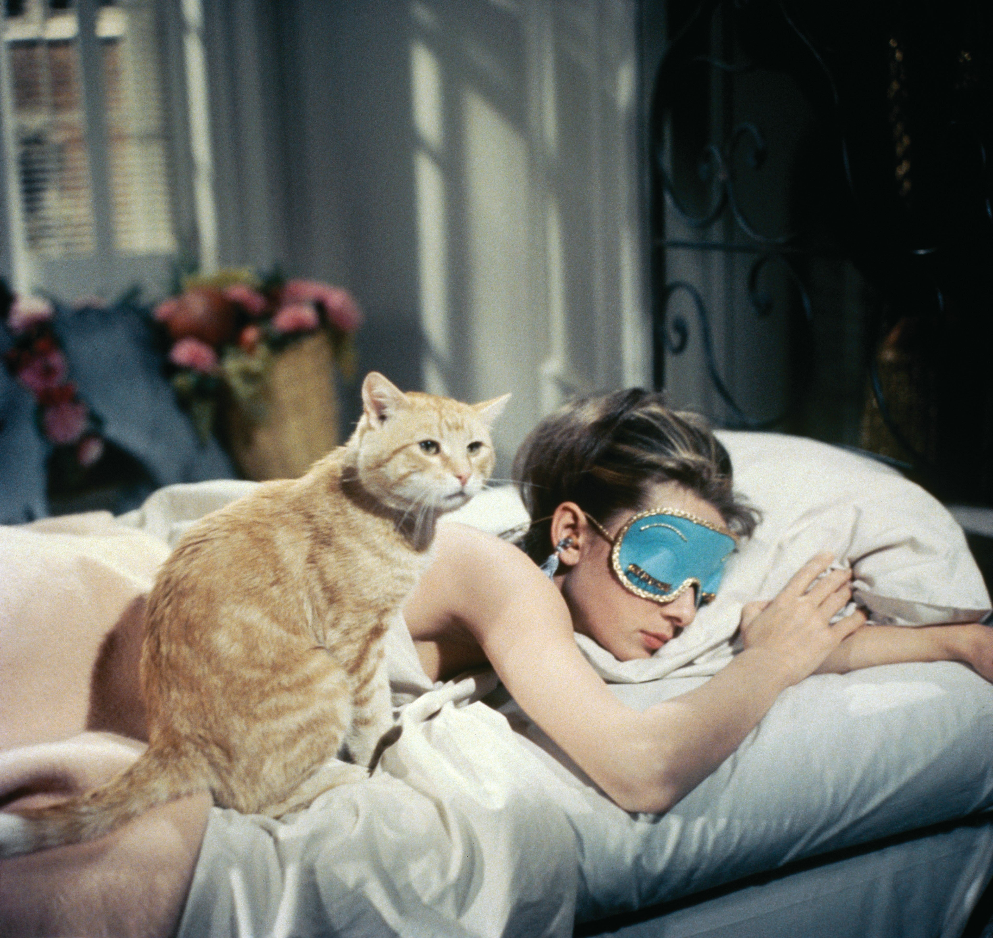 Woman sleeping on a bed with an eye mask, cat sitting beside her
