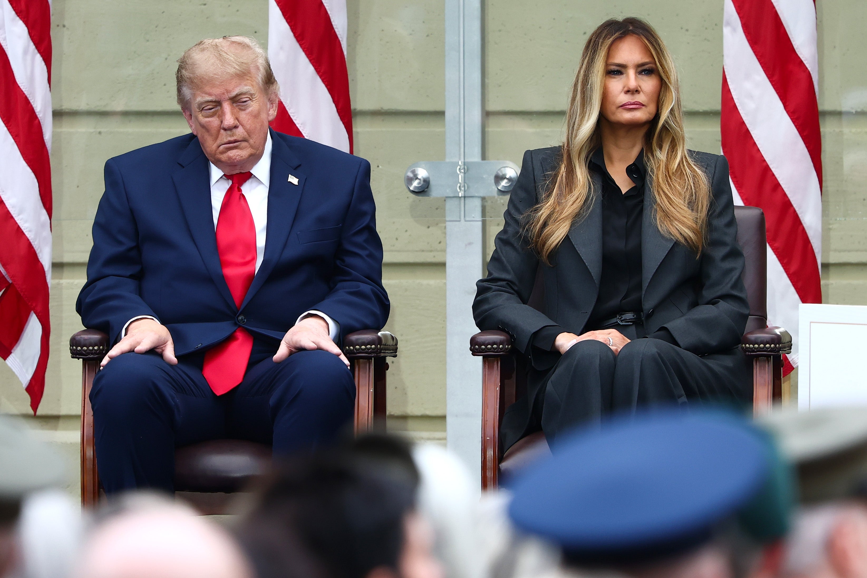 Donald Trump sitter ved siden av Melania på et arrangement, den ene i dress med rødt slips, den andre i mørkt antrekk. Øynene hans er nesten lukket