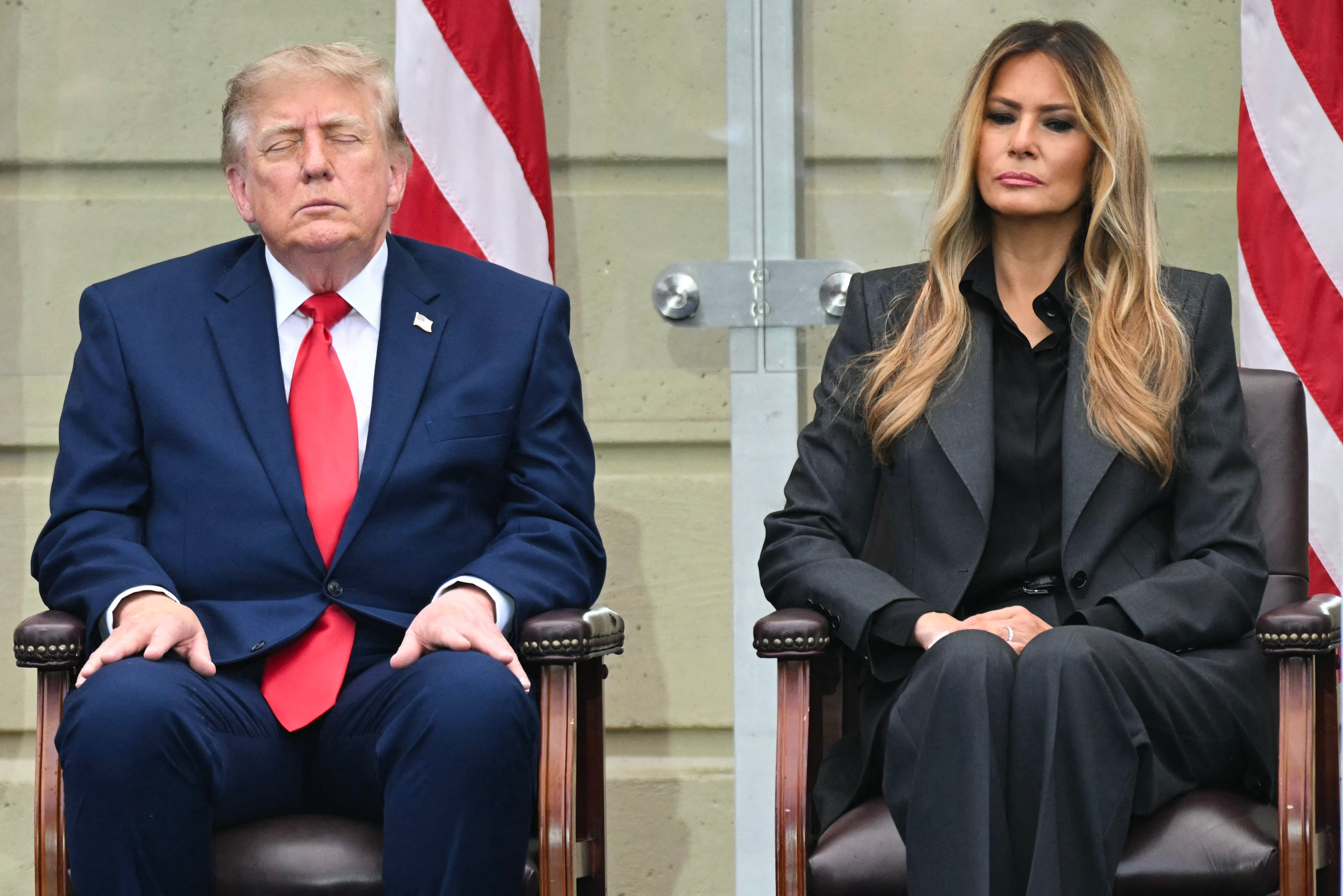 Donald og Melania Trump satt ved siden av hverandre på et arrangement; øynene hans er lukket. Amerikanske flagg er synlige i bakgrunnen