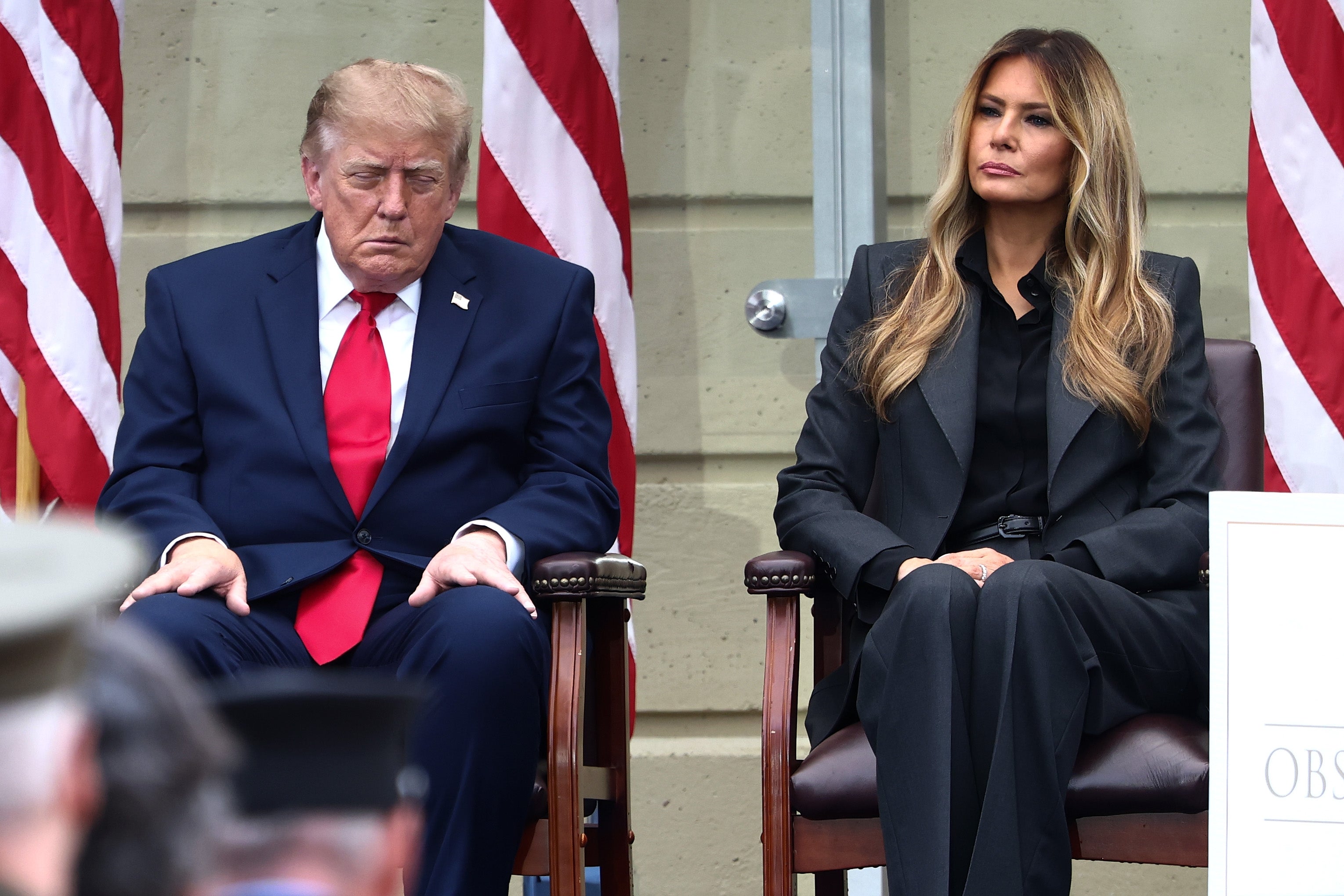 Donald Trump sitter ved siden av Melania på et arrangement, den ene i dress med rødt slips, den andre i mørkt antrekk. Øynene hans er nesten lukket