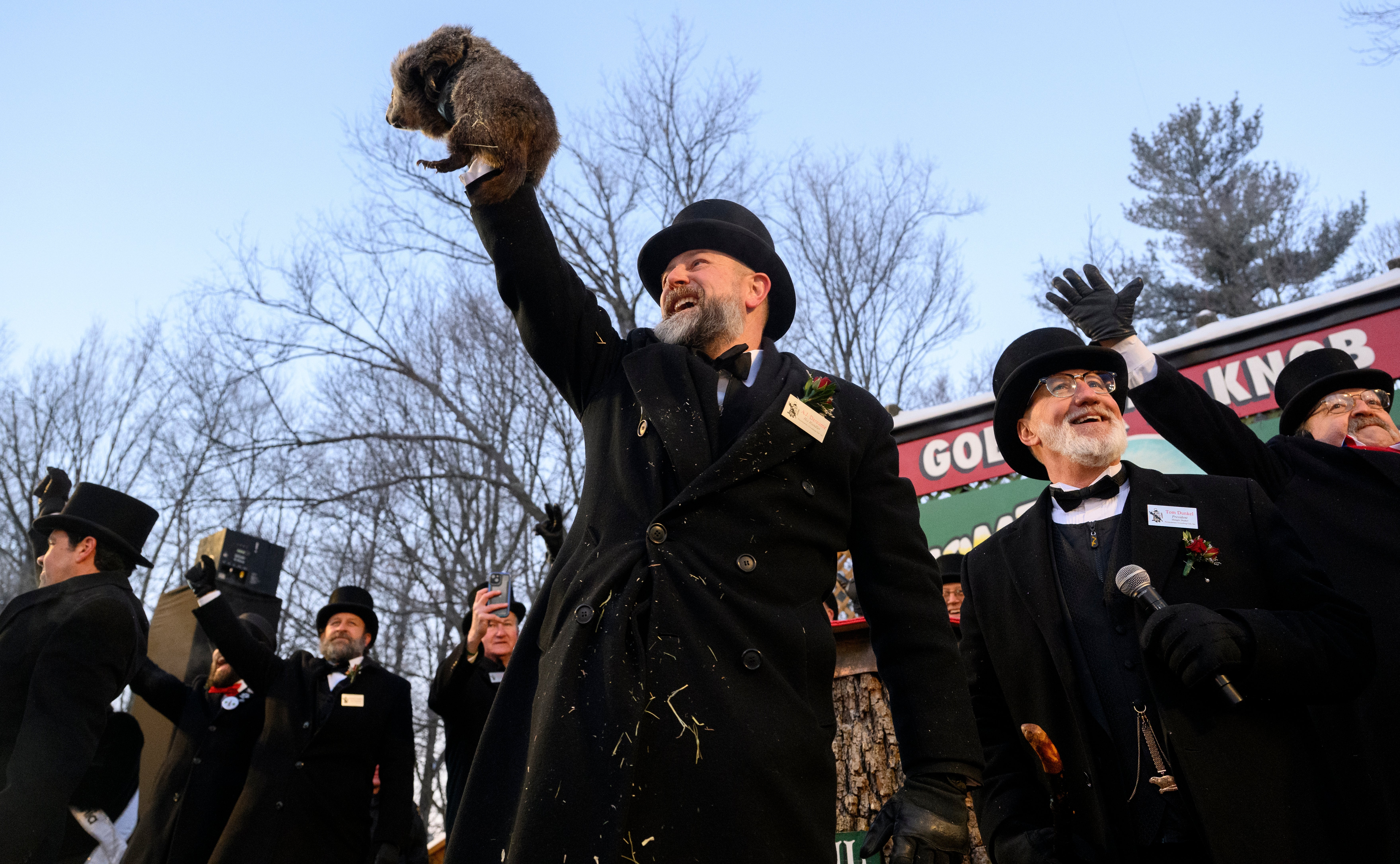 En mann i en formell frakk og hatt holder opp et jordsvin under tradisjonelle Groundhog Day-festligheter