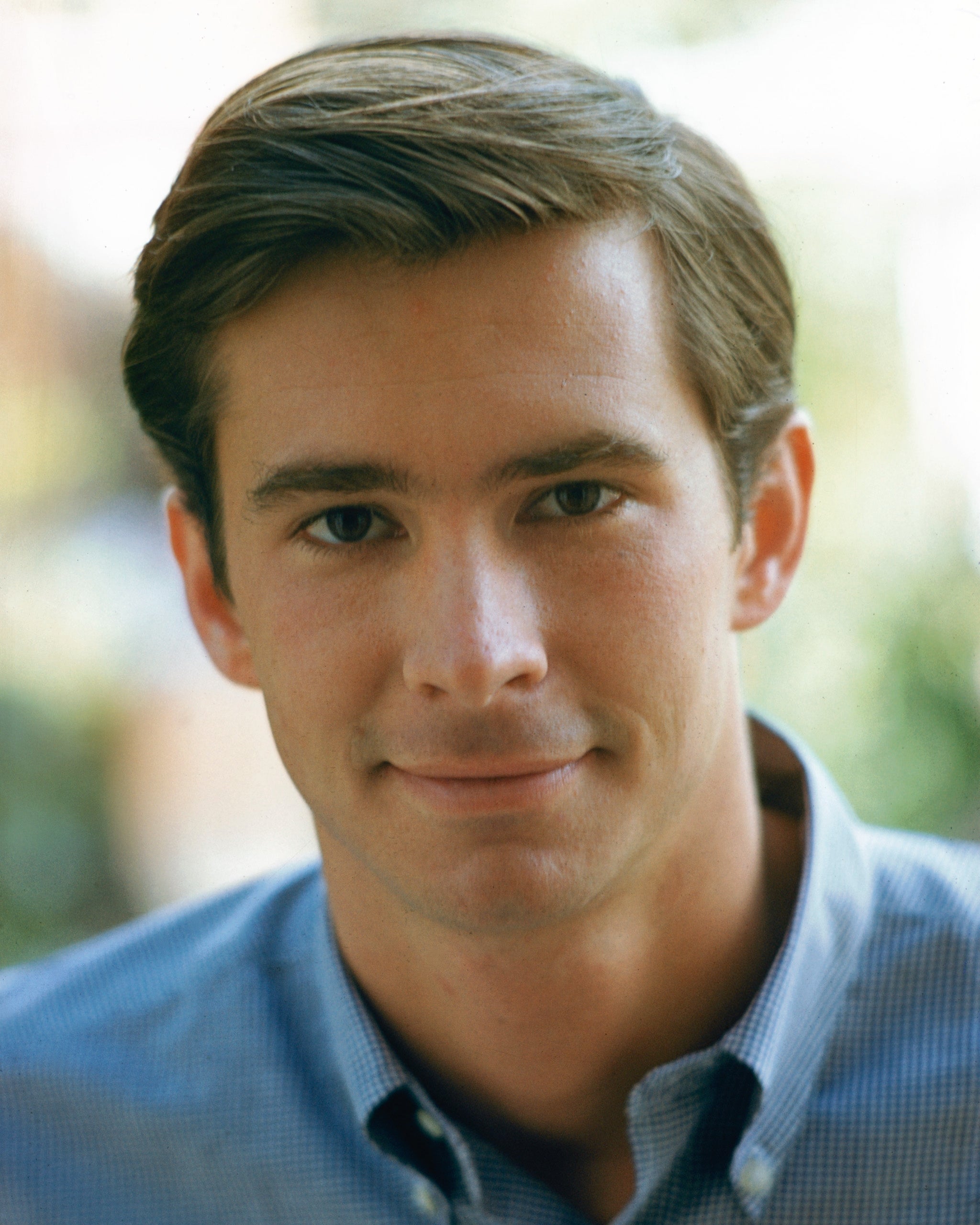 Portrait of a person wearing a collared shirt, smiling slightly, with neat, short hair. The background is softly blurred