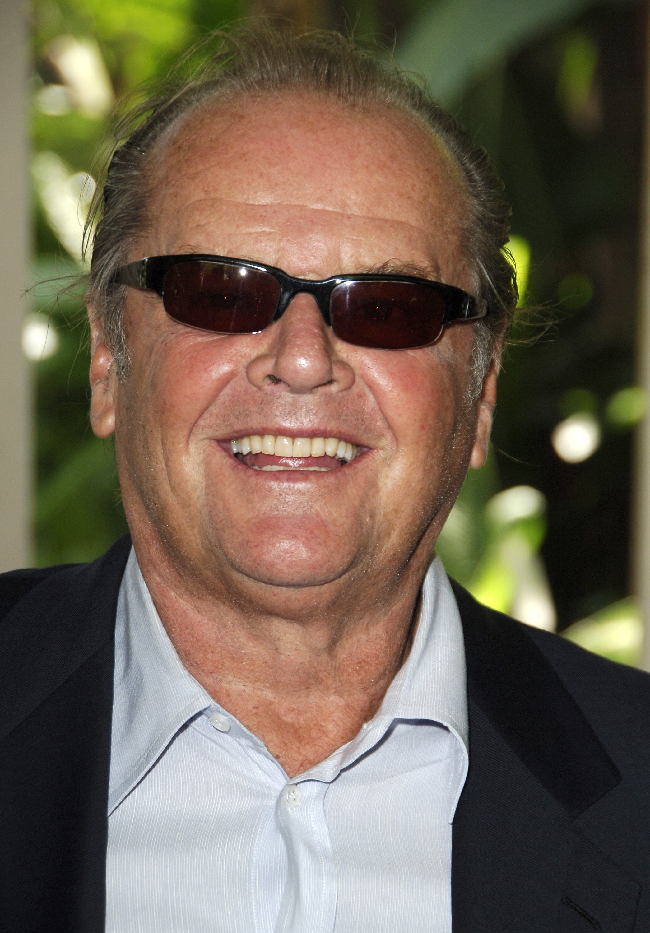 A person wearing sunglasses and a suit smiles at the camera