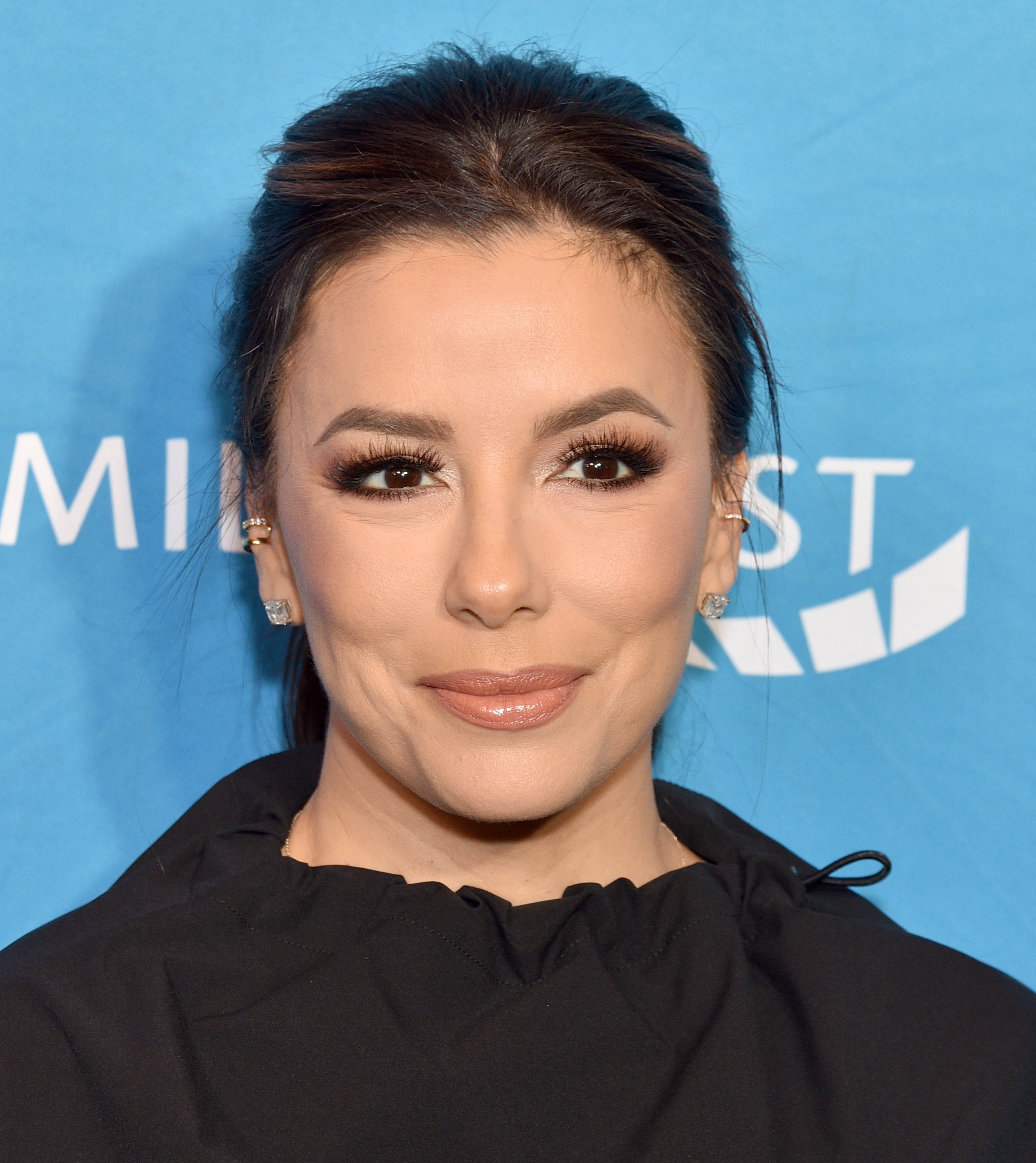 A person smiling at an event, wearing elegant evening attire with subtle makeup and styled hair